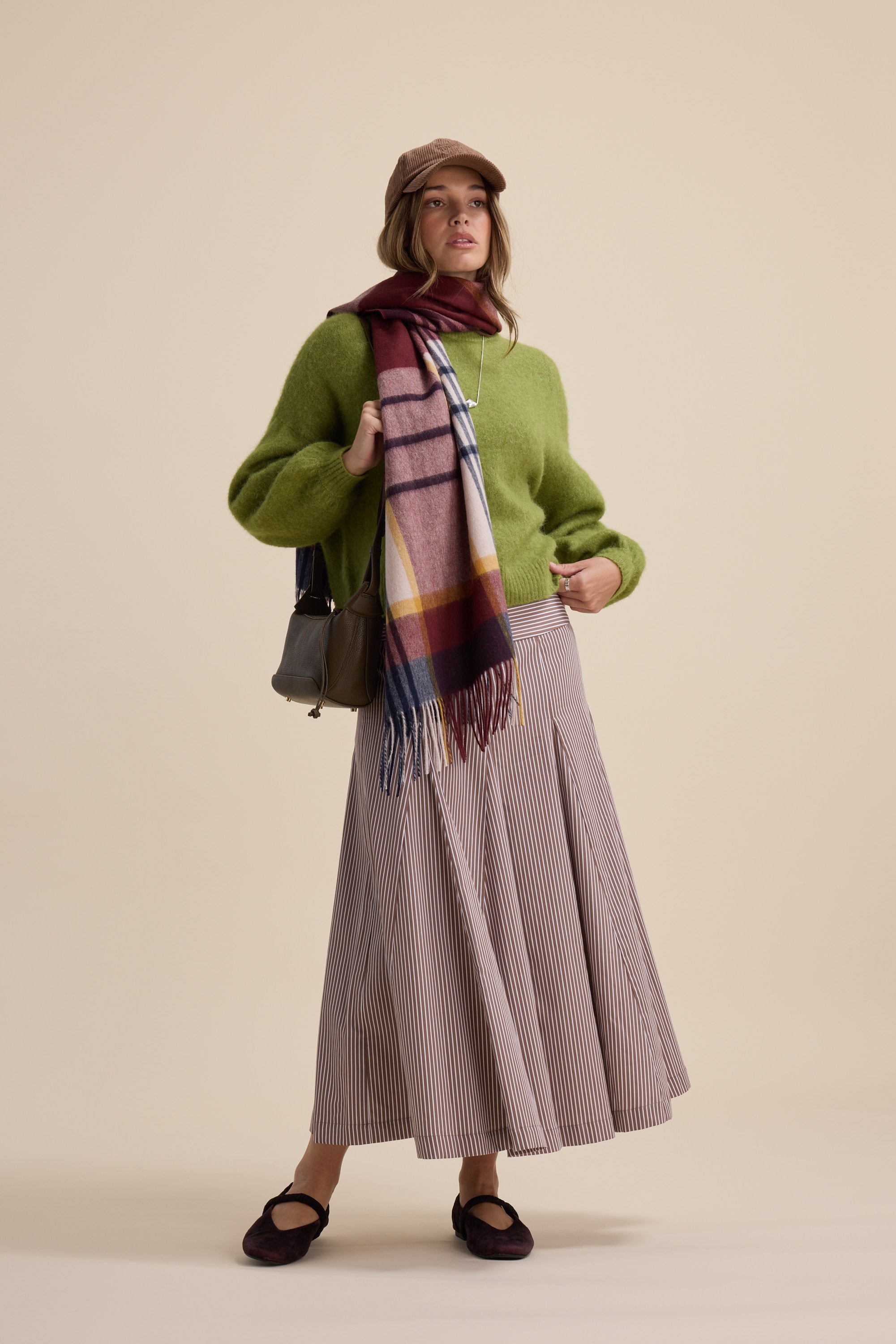 Woman in green sweater, Max Marley Panel Seam Skirt, scarf, cap, flats, and handbag.