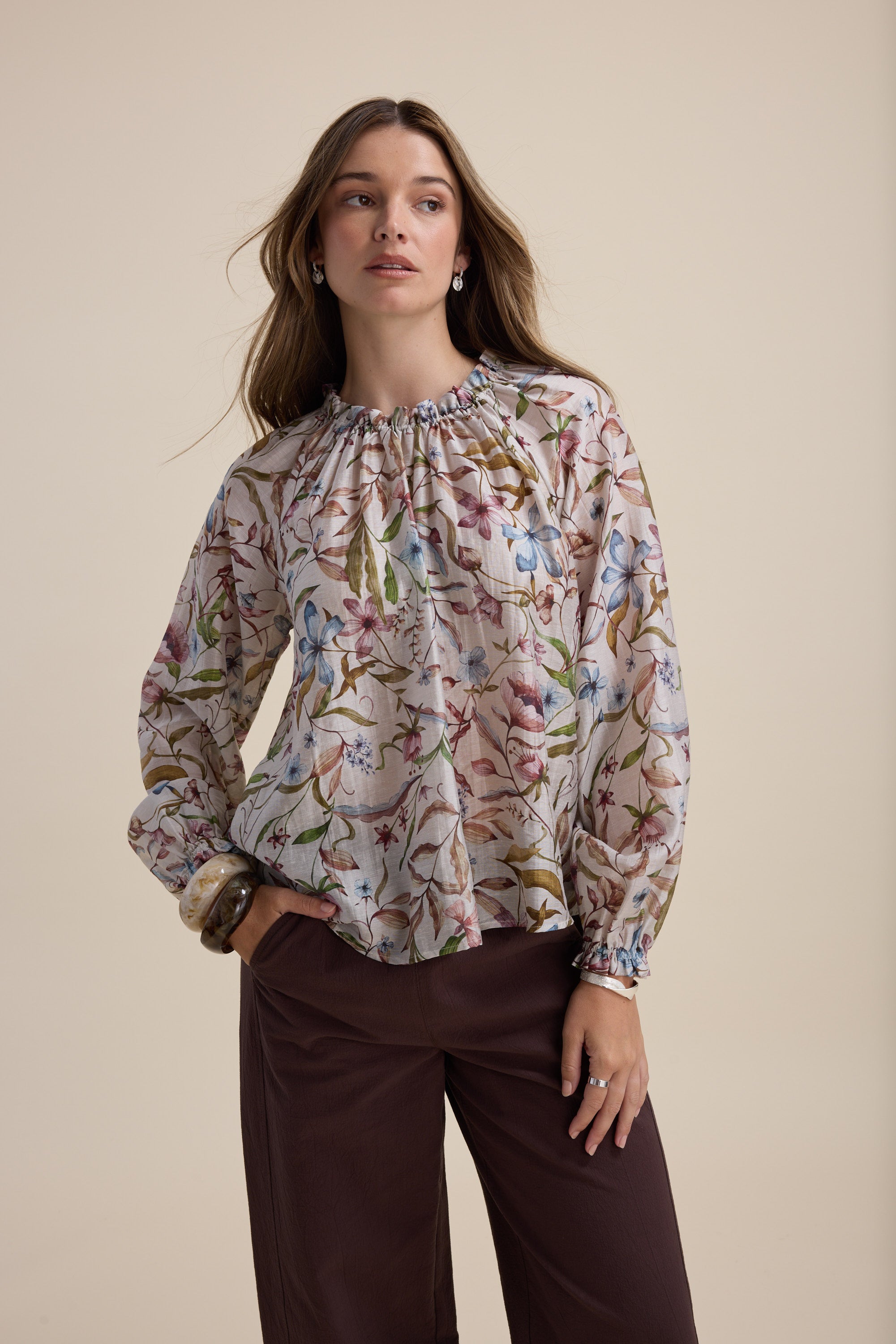 Woman in Max Quinn Gather Detail Blouse and brown pants, posing against a beige background.
