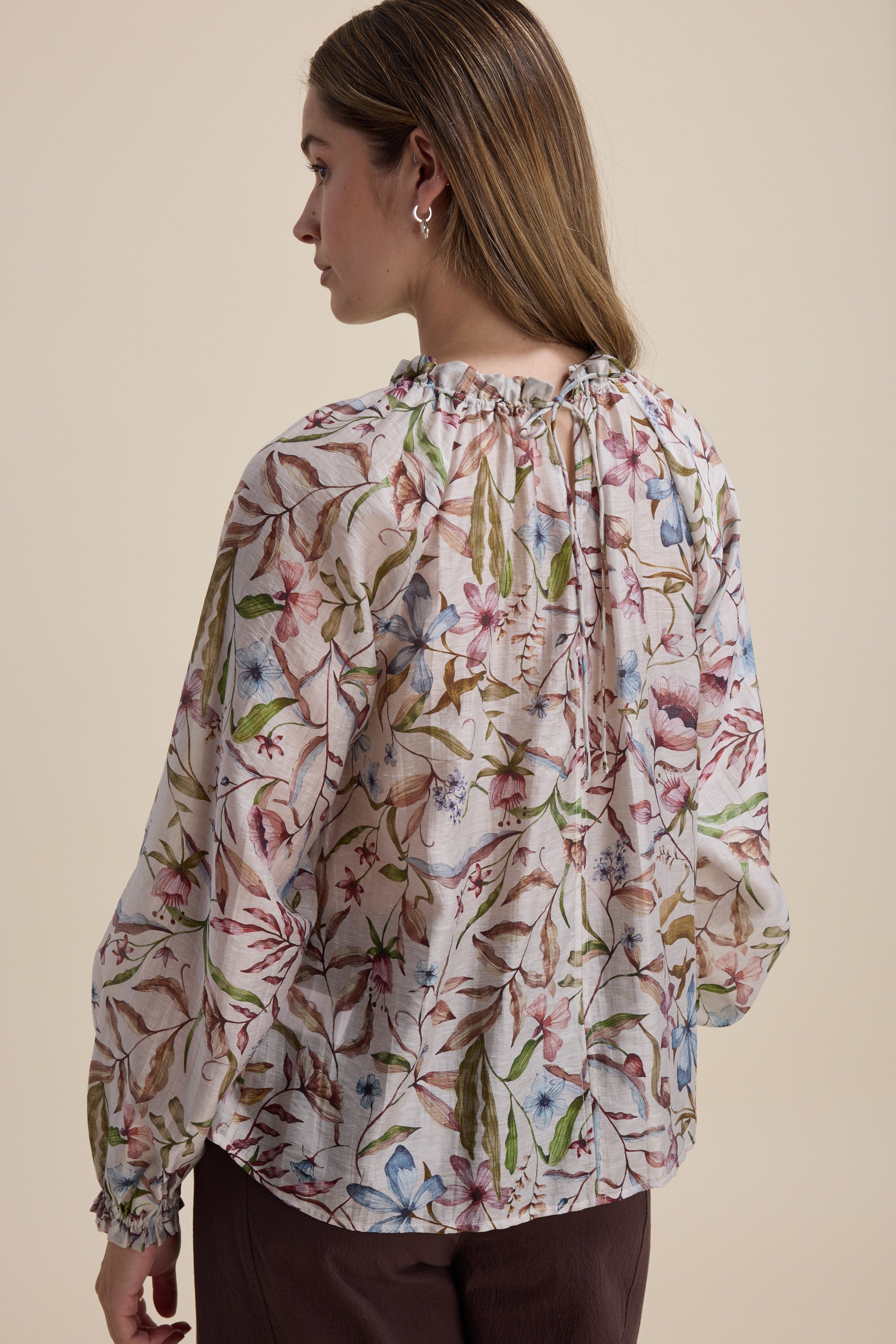 Woman wears the Max Quinn Gather Detail Blouse, floral print, seen from the back on beige.