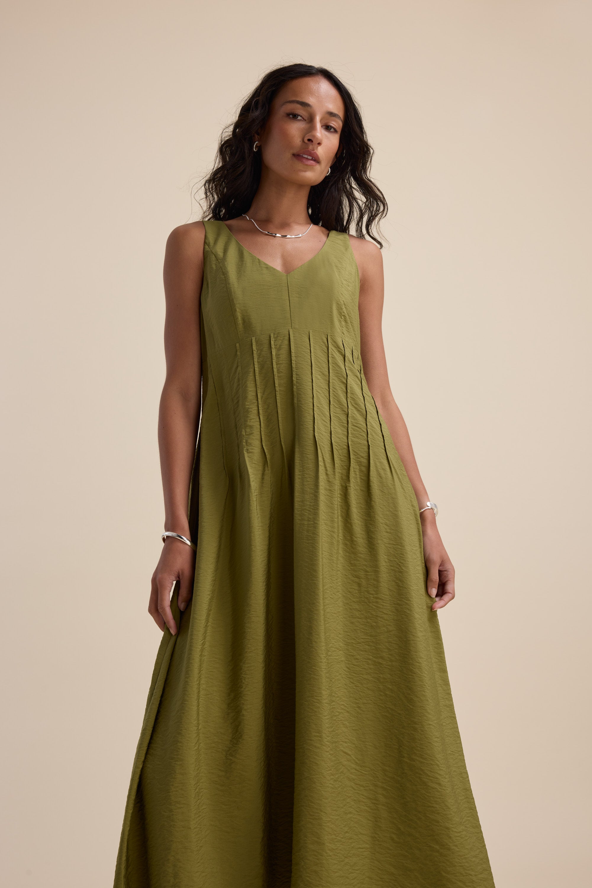 Woman in Max's Nina Fit and Flare Dress, sleeveless dill green, against a beige background.