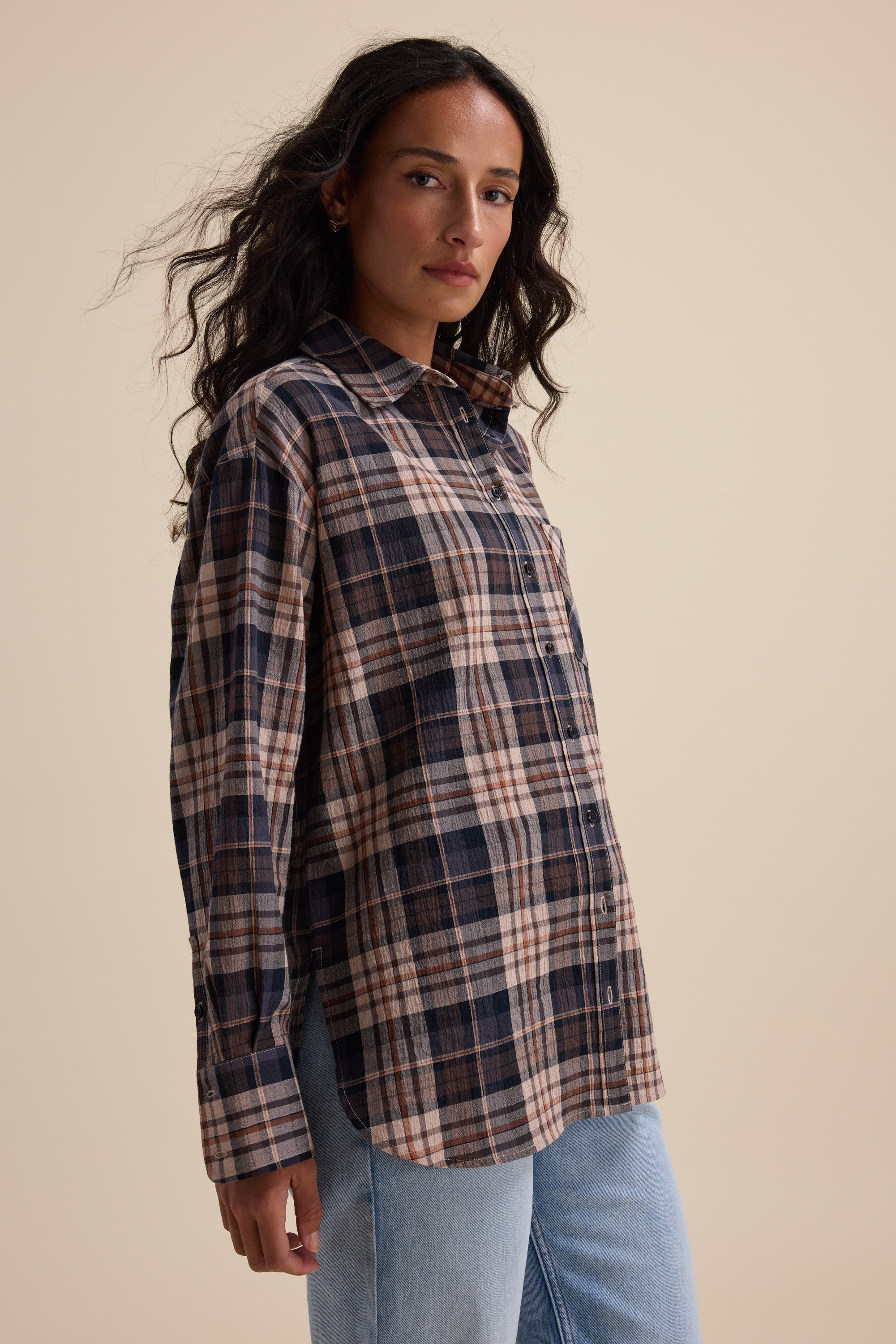 Woman in an Elementary Textured Shirt and light blue jeans, posed against a beige background.