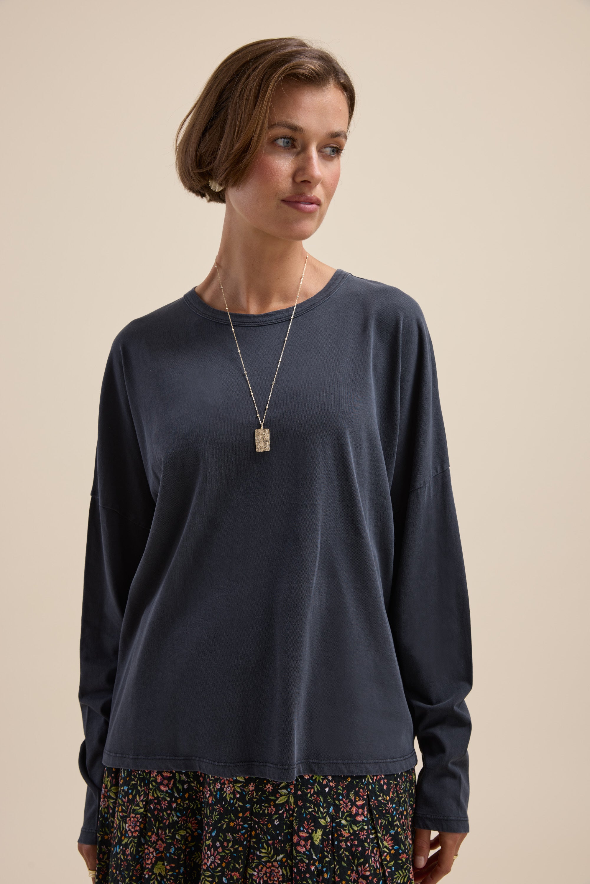 Woman in Max Elementary Slouchy Long Sleeve Tee and floral skirt with a pendant necklace, looking left.