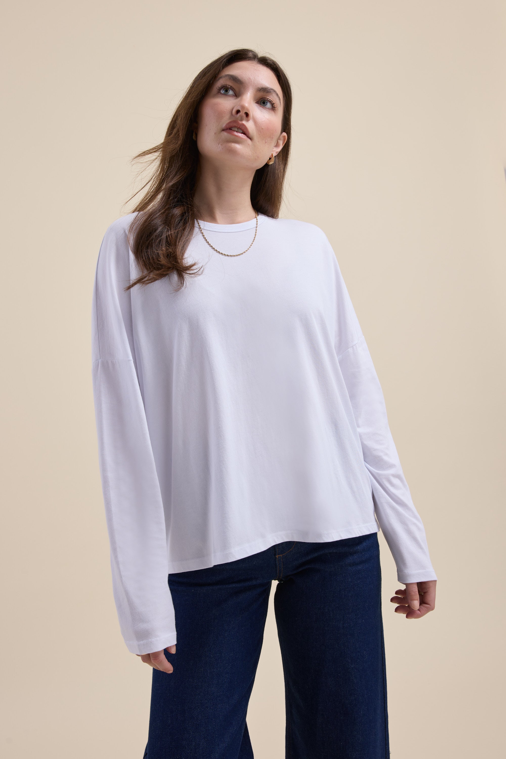 Woman in Max's Elementary Slouchy Long Sleeve Tee and dark jeans on a beige background.