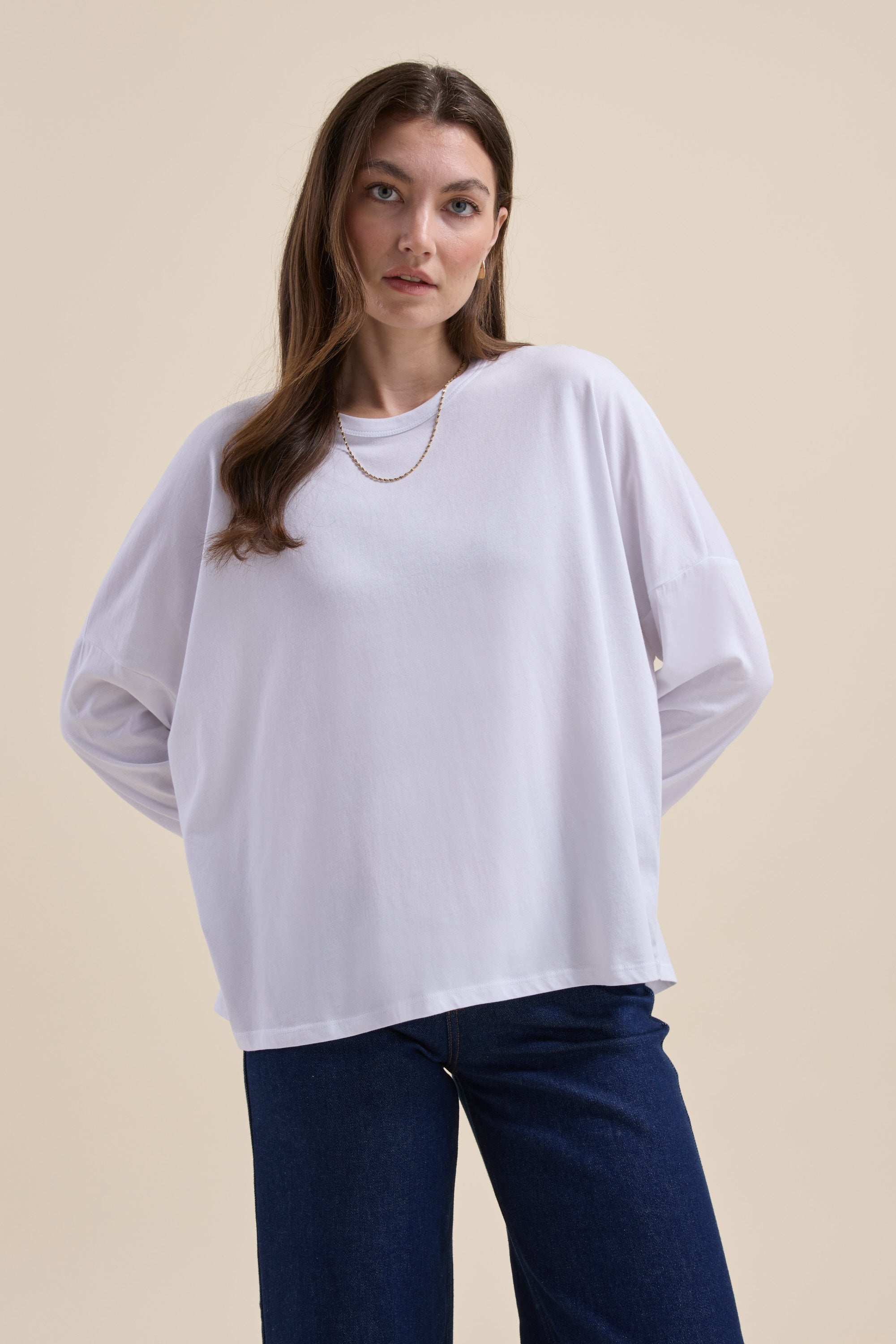 Woman wears Max Elementary Slouchy Long Sleeve Tee and dark jeans against a beige background.