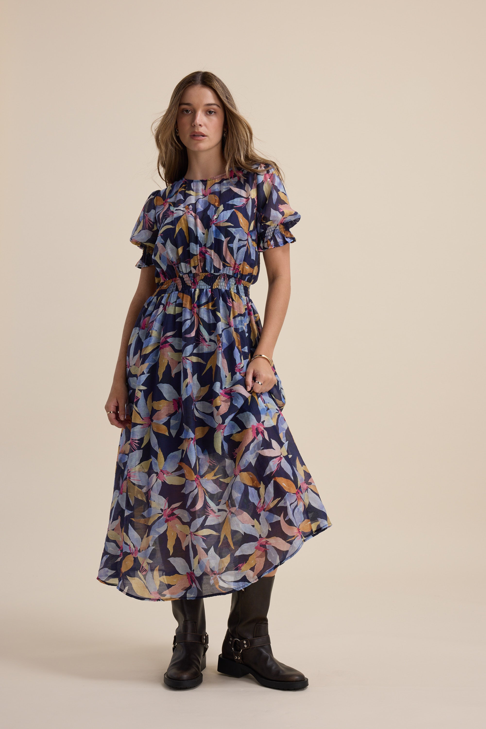 Woman in Max Ava Gather Waist Dress with puff sleeves and black boots on beige background.