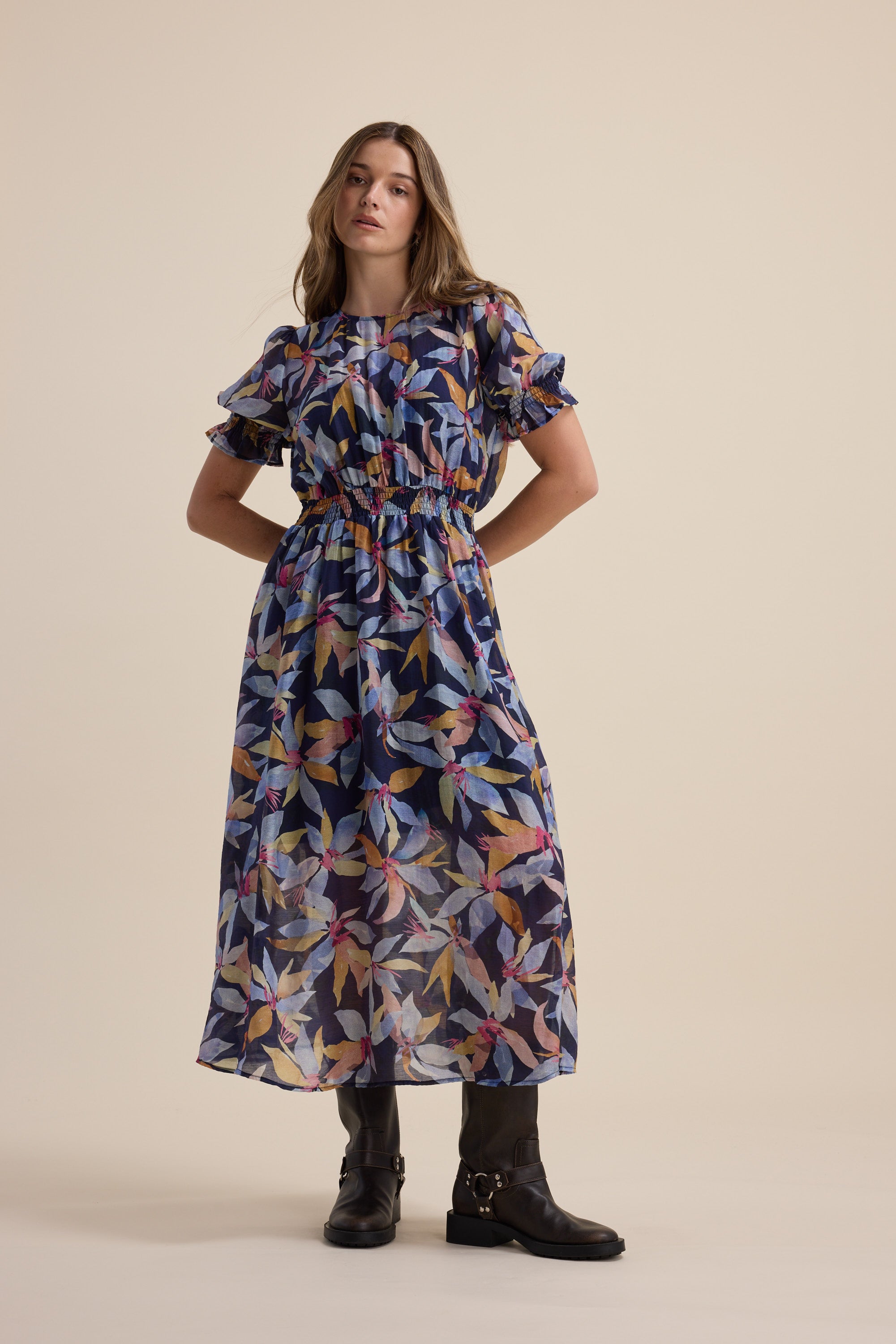 Woman in an Ava Gather Waist Dress by Max and black boots stands against a plain background.