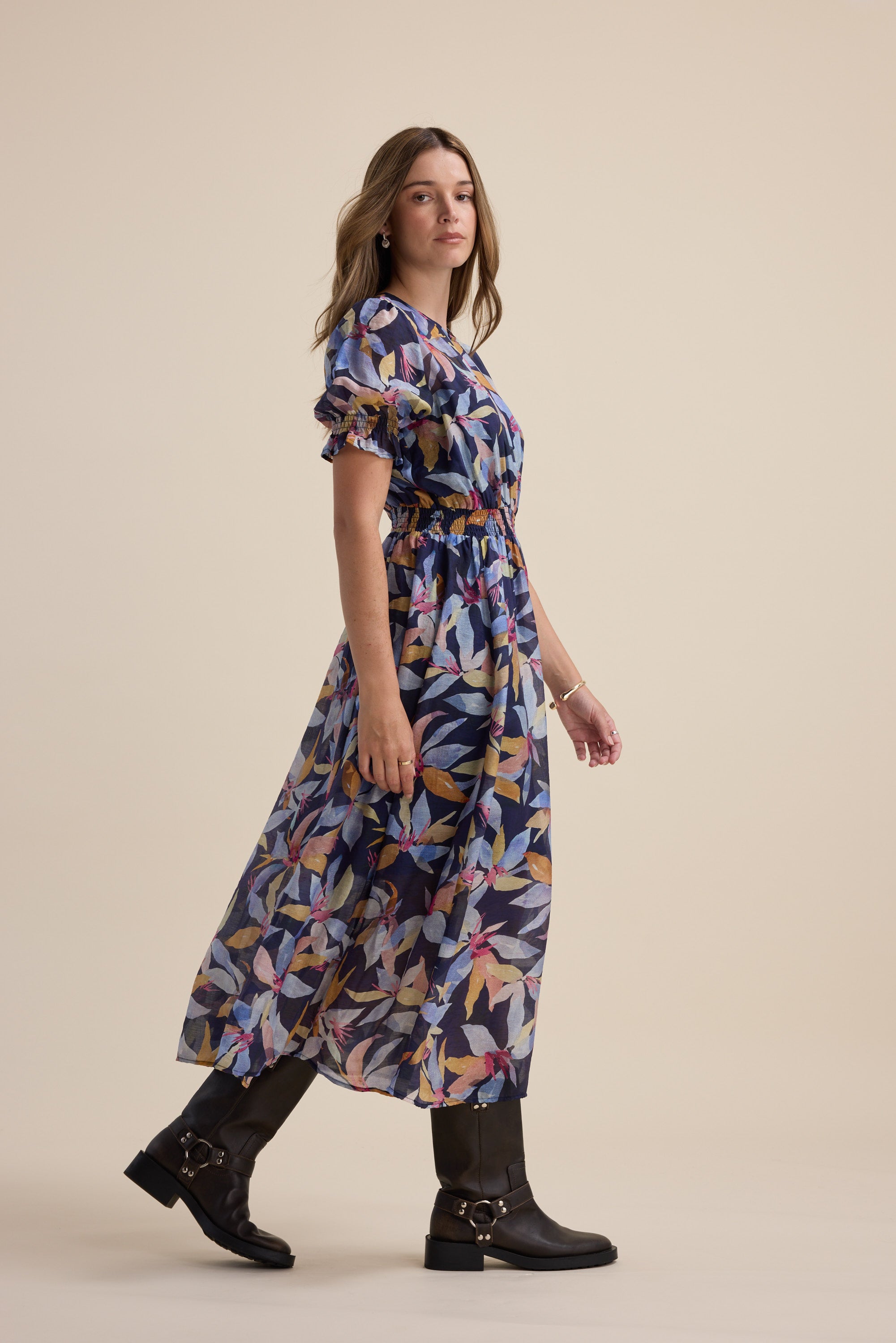 Woman in the Max Ava Gather Waist Dress with puff sleeves and black boots against a beige background.