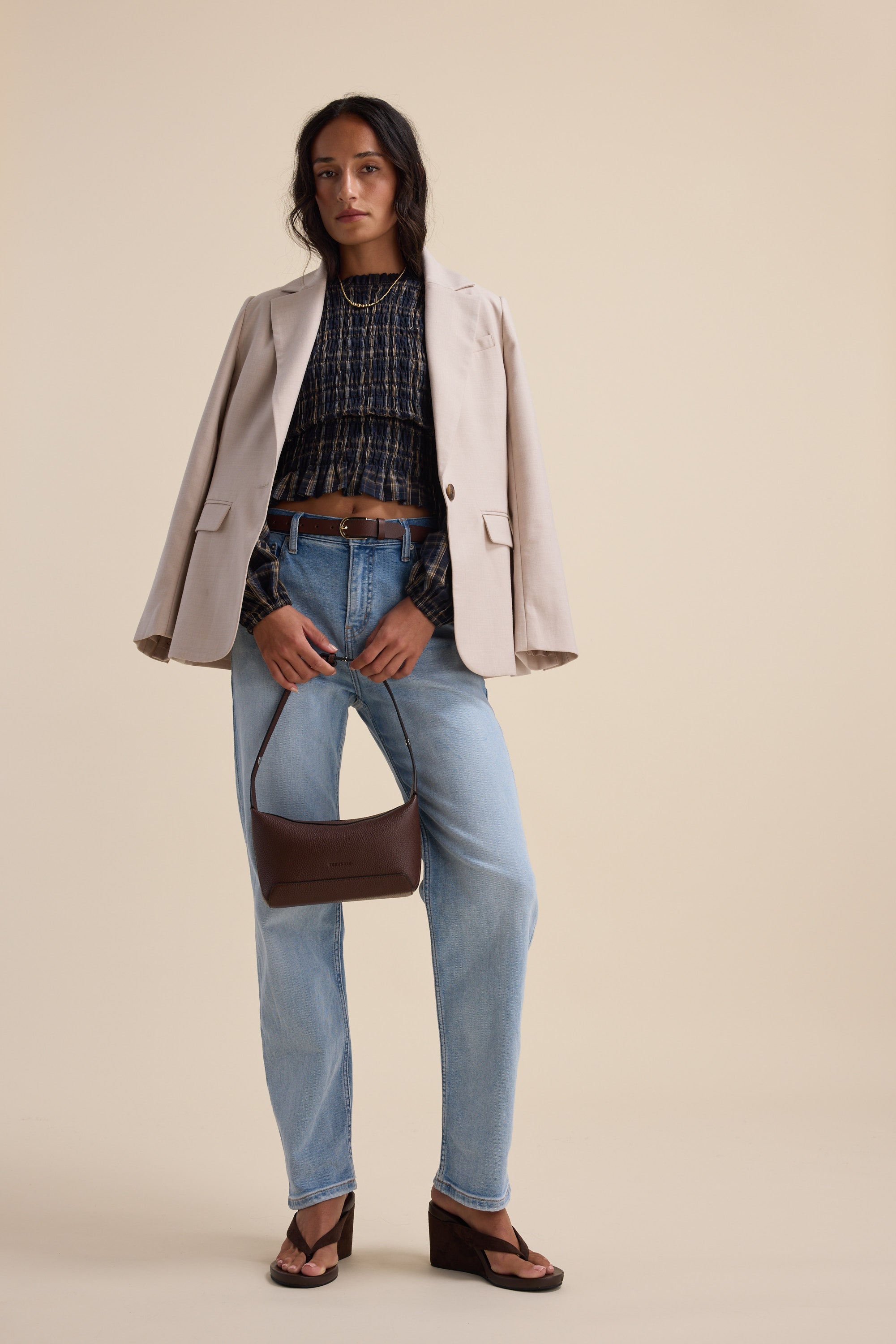 Woman in a beige blazer, Elementary Shirred Long Sleeve Top, jeans, sandals, with brown purse.