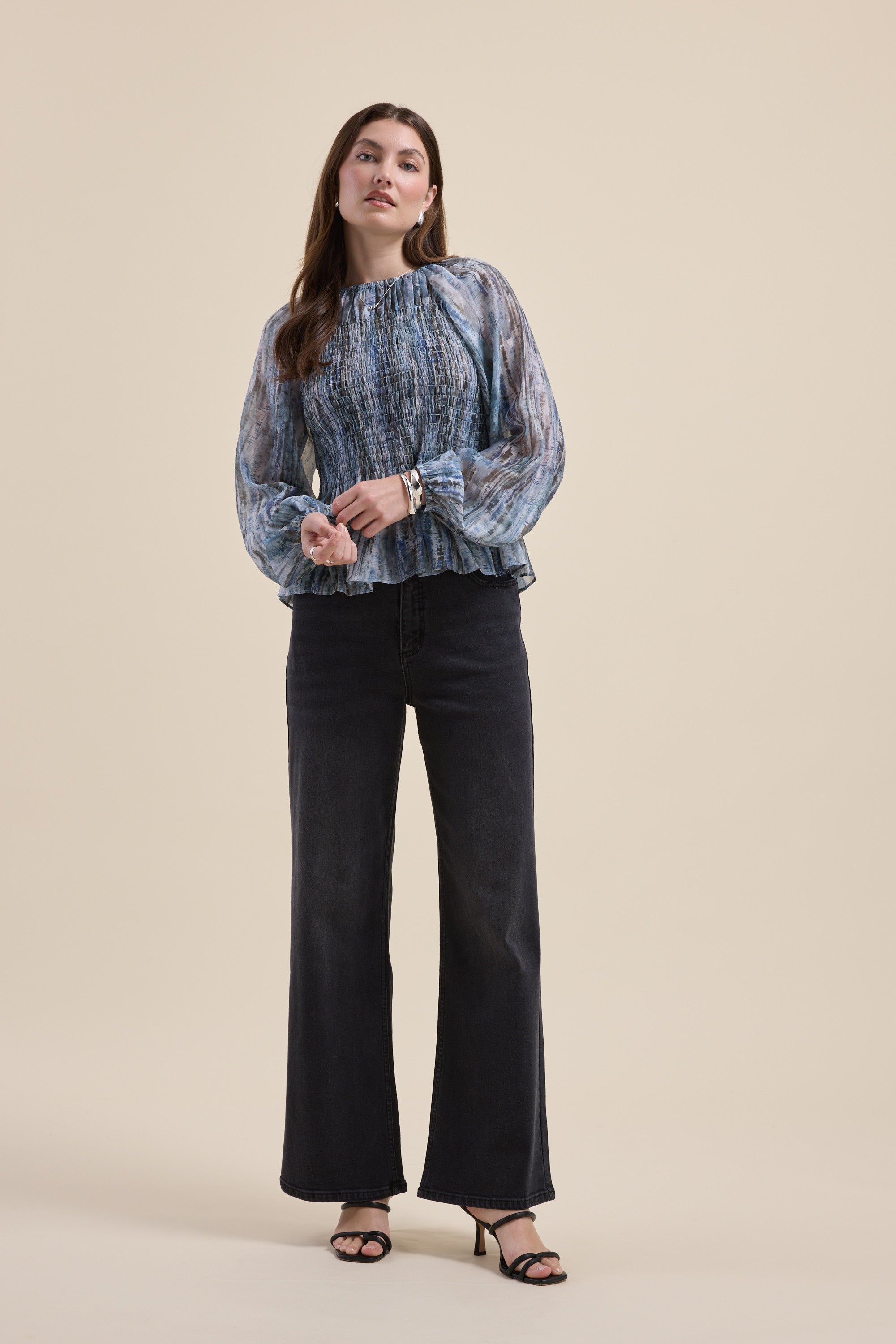 Woman in Max Mitch Shirred Top and black wide-leg jeans against a beige background.