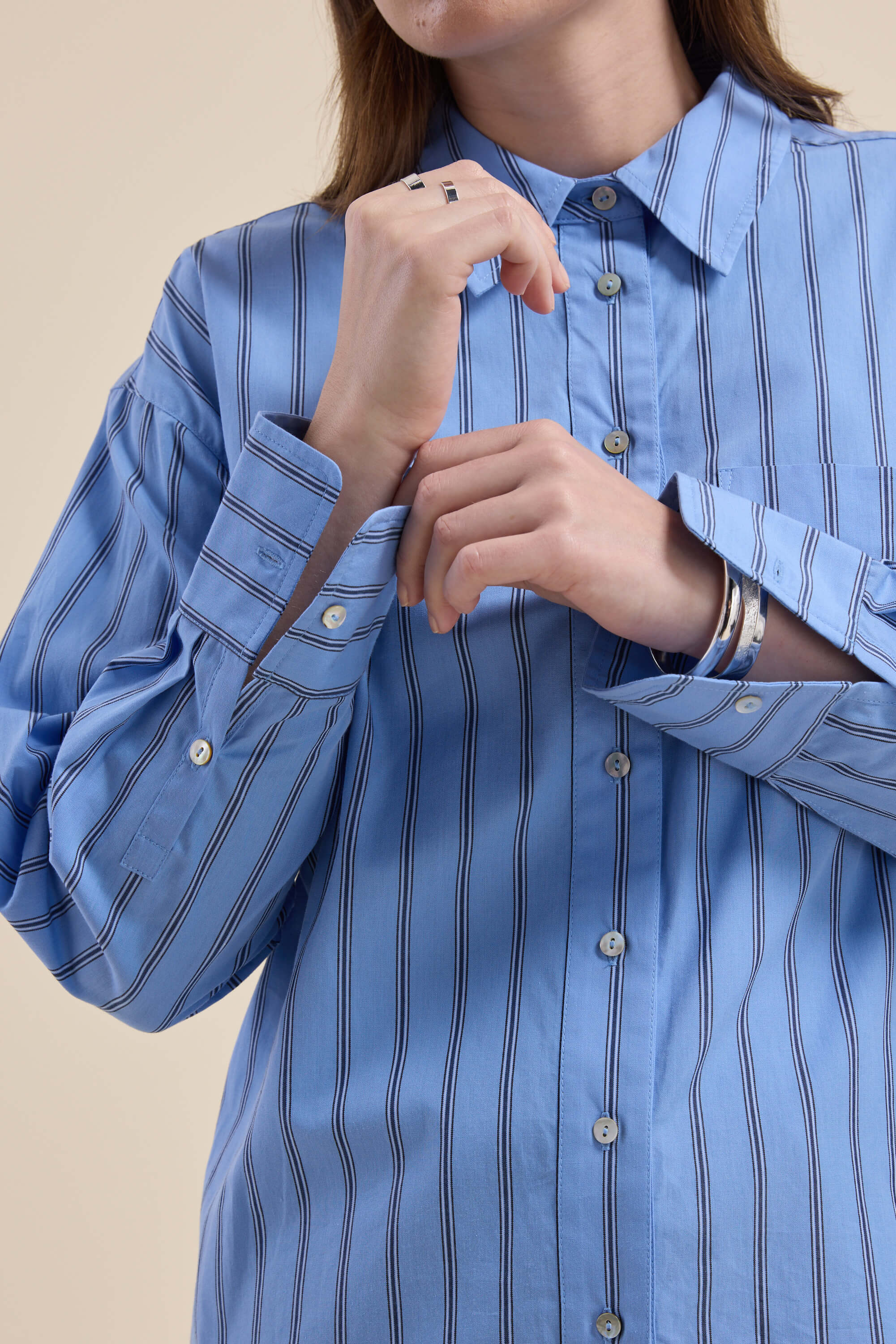 Person in Max Cameron Oversized Shirt, blue stripes, buttoning cuff with rings and a bracelet.