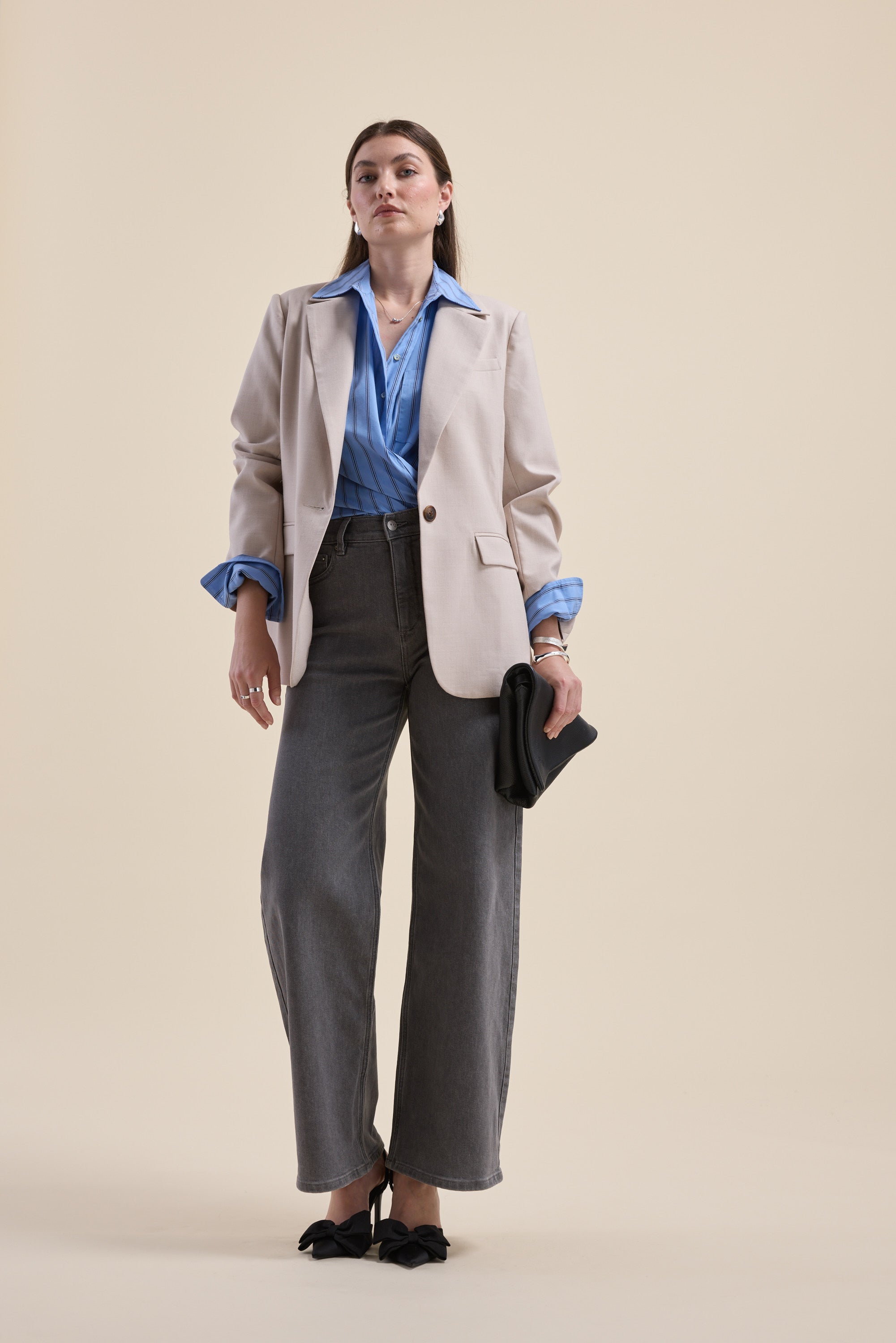 Woman in a Max Cameron Oversized Shirt, blazer, gray pants, heels, holding a black clutch.