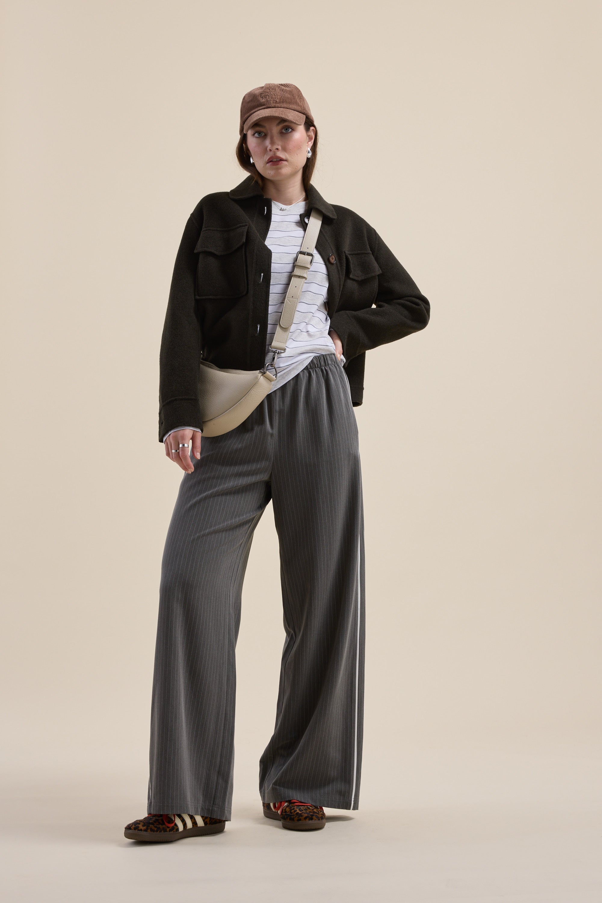 Woman in Carmen Long Sleeve Stripe Tee by Max, wide-leg pants, black jacket, cap, and crossbody bag.