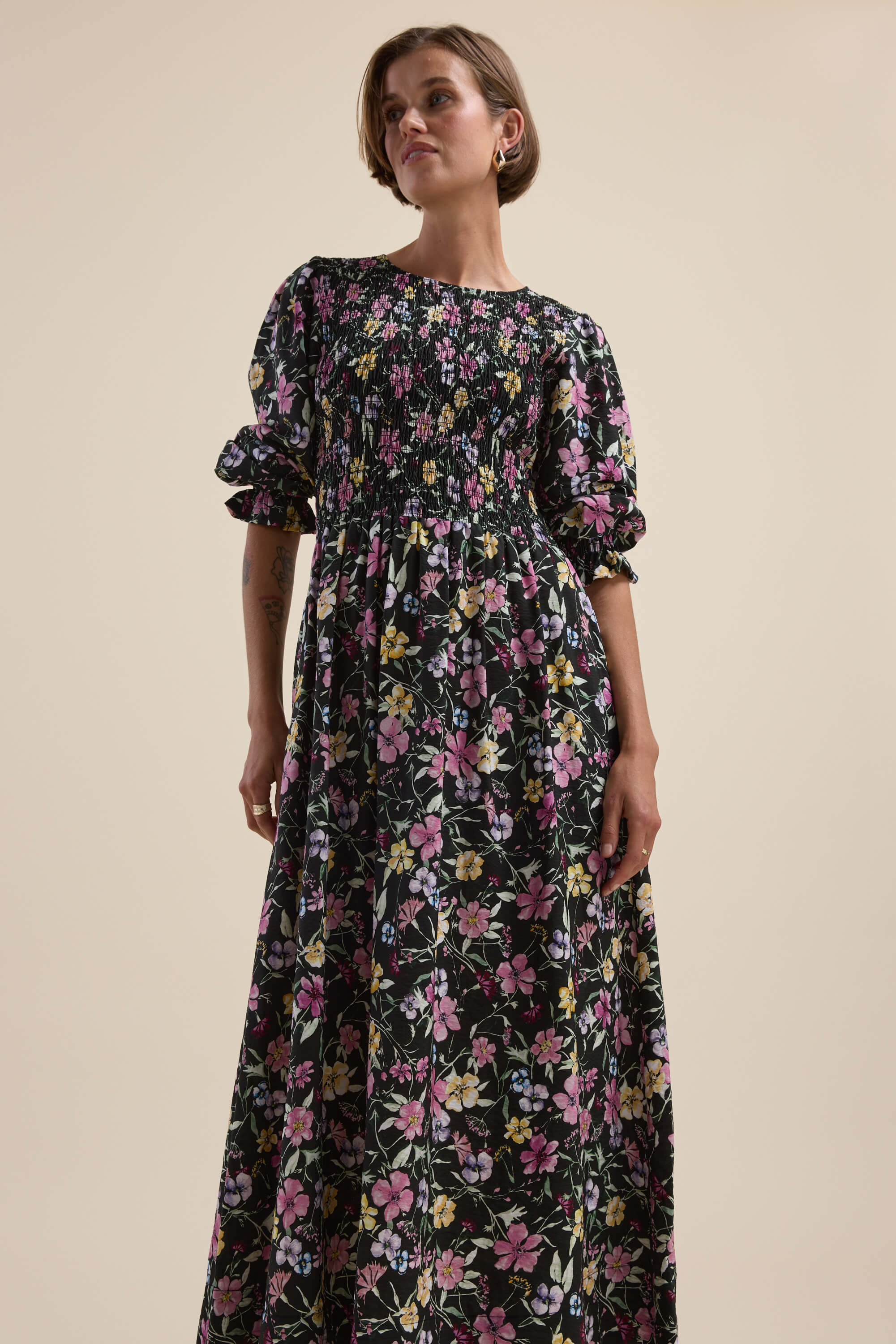 Woman in Max’s Brooke Shirred Long Sleeve Dress, black, with puffed sleeves on beige backdrop.