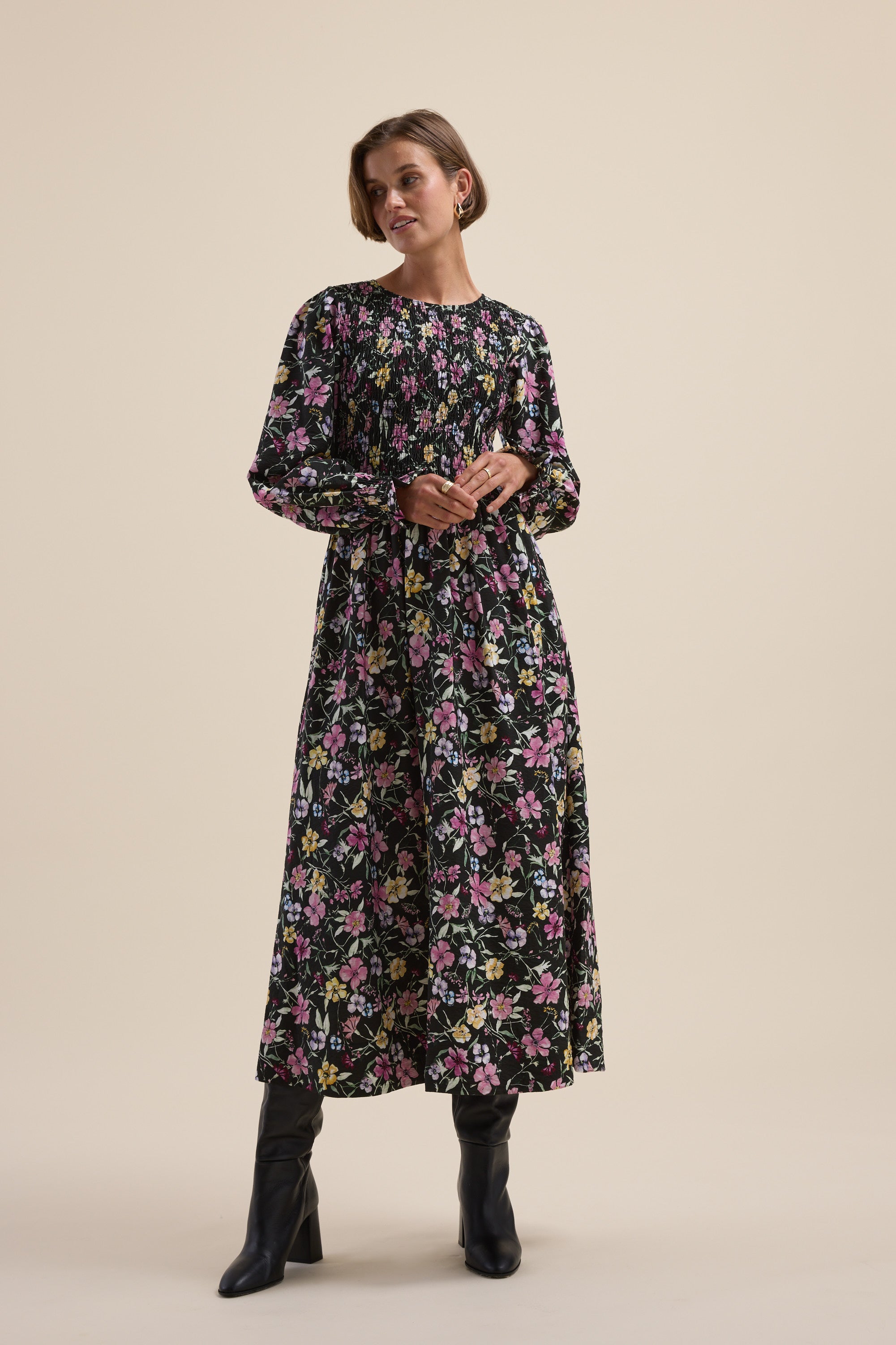 Woman in the Max Brooke Shirred Long Sleeve Dress and black boots against a beige background.