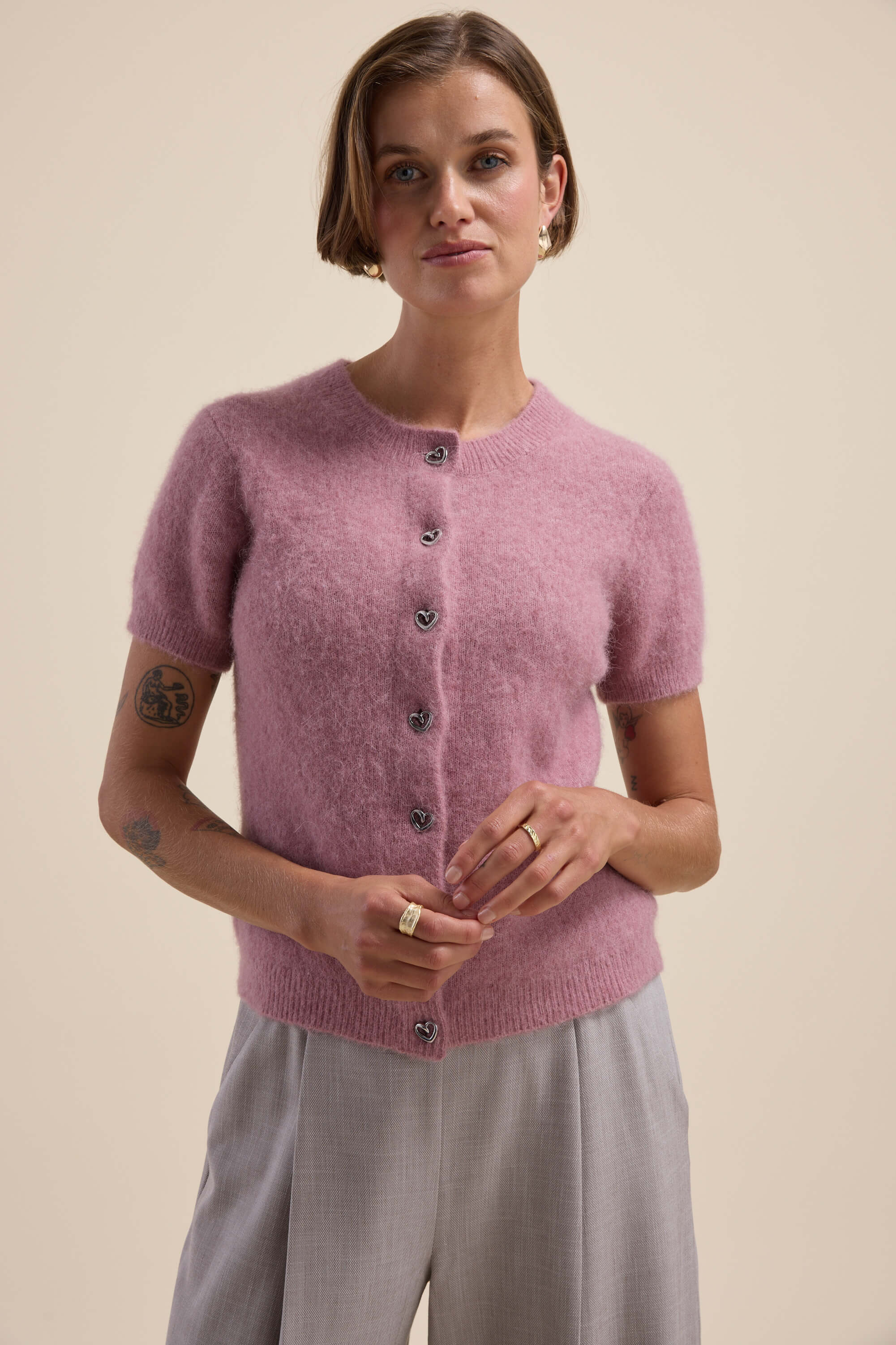 Woman in a pink Max Adelaide Luxe Whisper Short Sleeve Cardigan and gray pants on beige background.