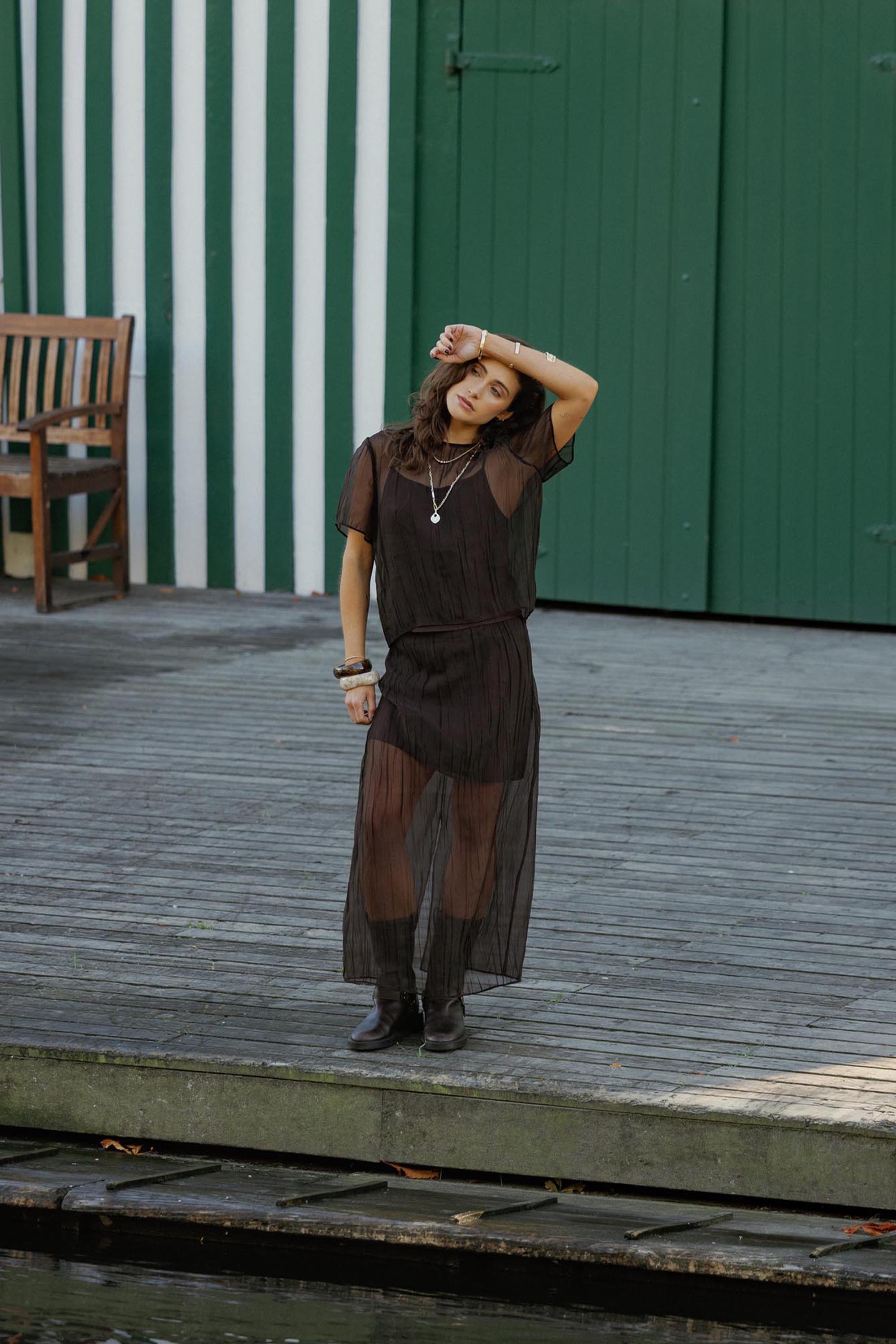 Max Cass Sheer Top worn by woman on dock near green and white striped doors.