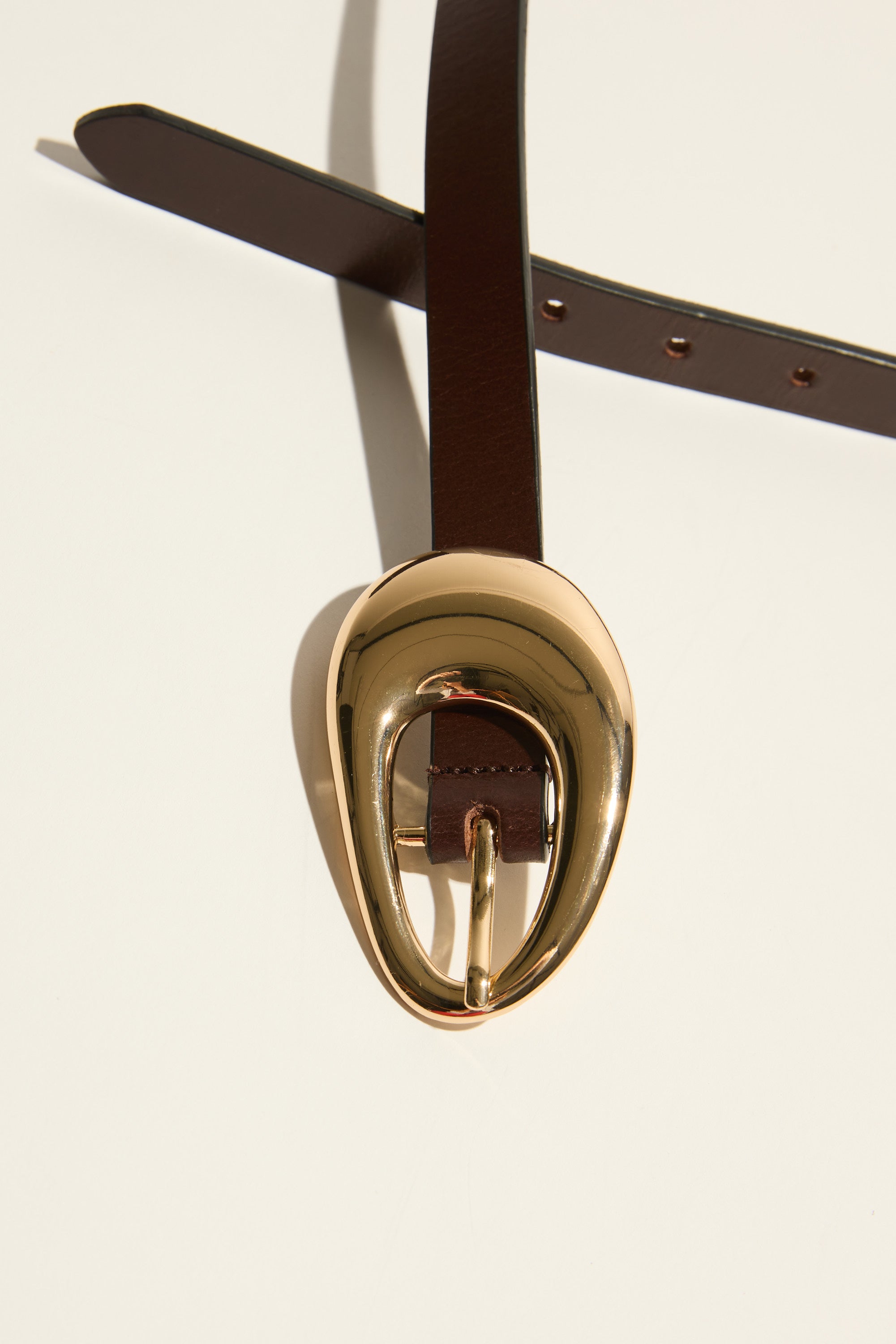 Max Chelsea Oval Buckle Slim Belt in dark brown with a gold buckle on a light background.