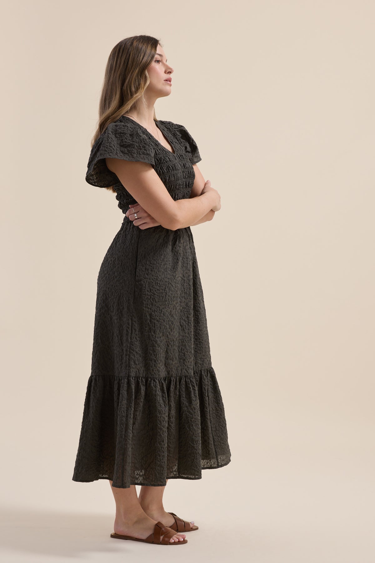 Woman in an Elementary Shirred Bodice Dress and sandals stands with arms crossed, facing left.