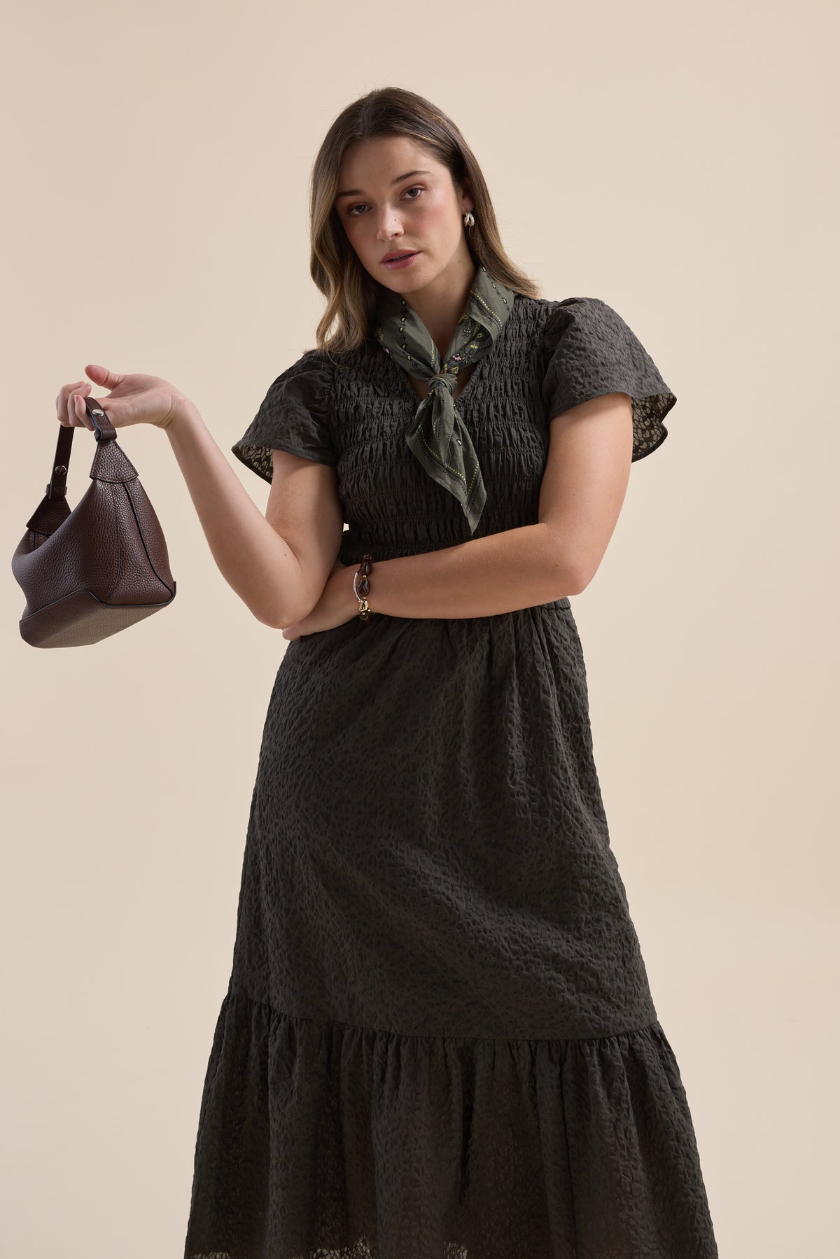 Woman in an Elementary Shirred Bodice Dress, holding a brown bag, with green scarf.