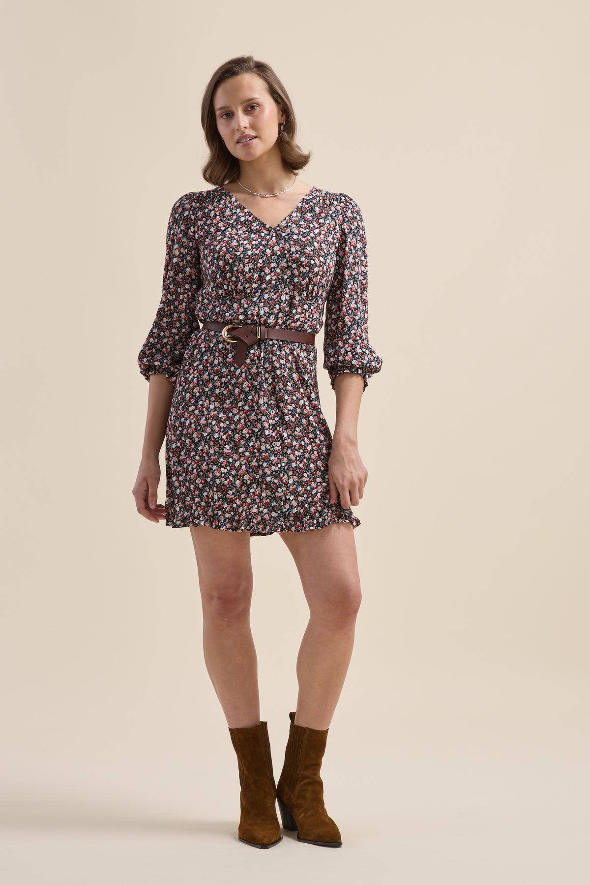 Woman in an Elementary Button Front Dress and brown boots stands against a beige background.
