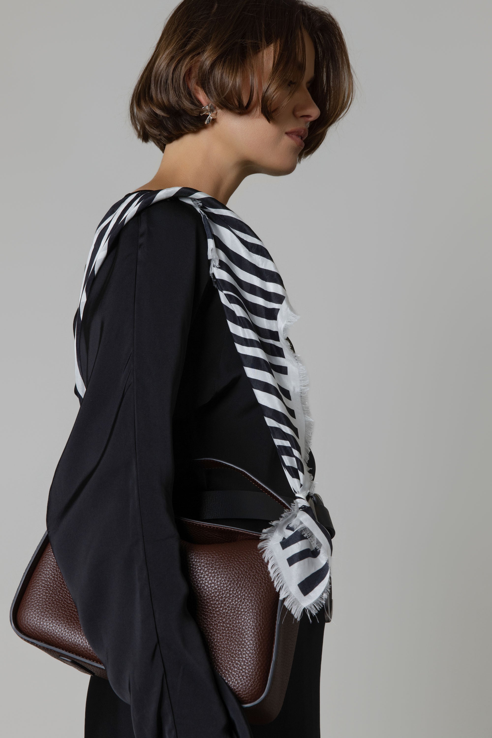 Woman in black with Max’s Mable Frayed Edge Silk Scarf and brown handbag against a plain background.
