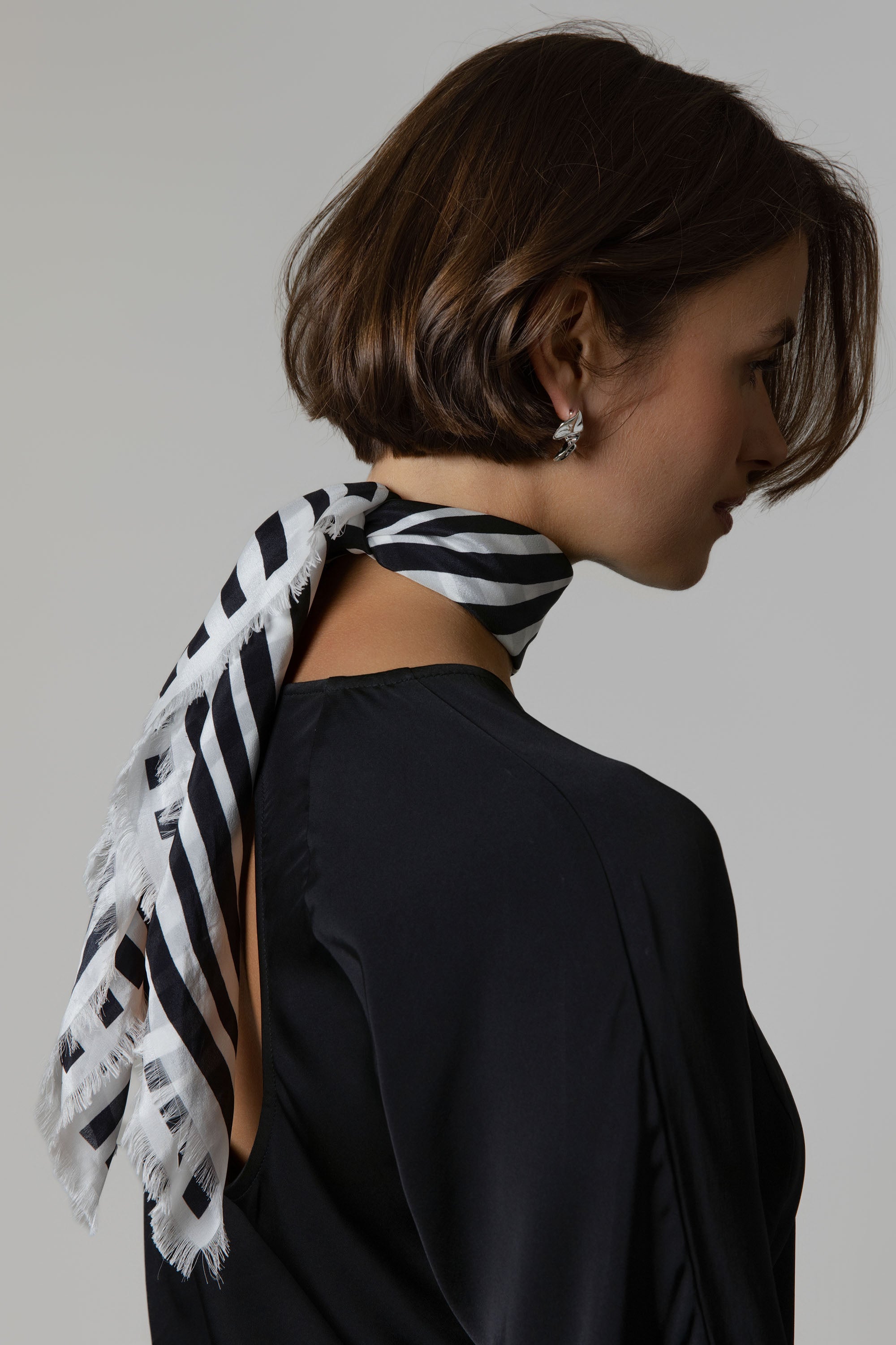 Woman wearing Max Mable Frayed Edge Silk Scarf around her neck, side view, black top.