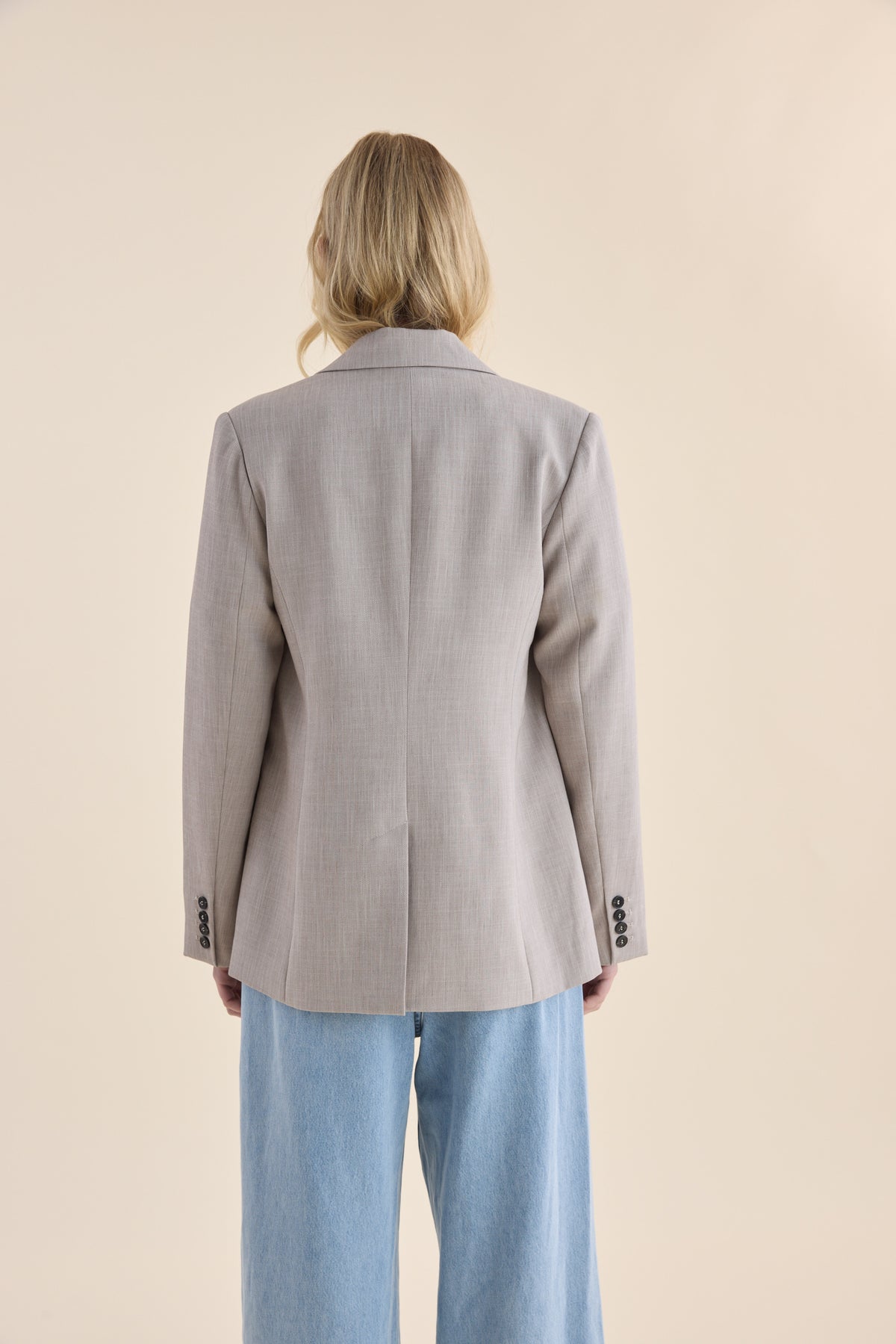 Blond person in Max’s The Relaxed Blazer and blue jeans, shown from the back, neutral background.