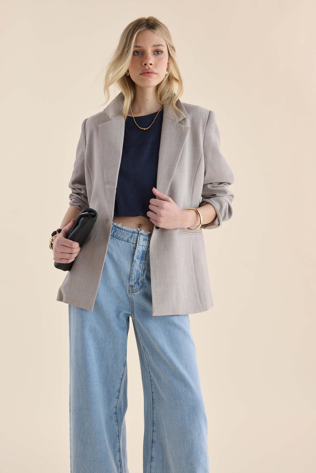 Woman in Max’s The Relaxed Blazer, black top, blue jeans, with clutch, standing confidently.