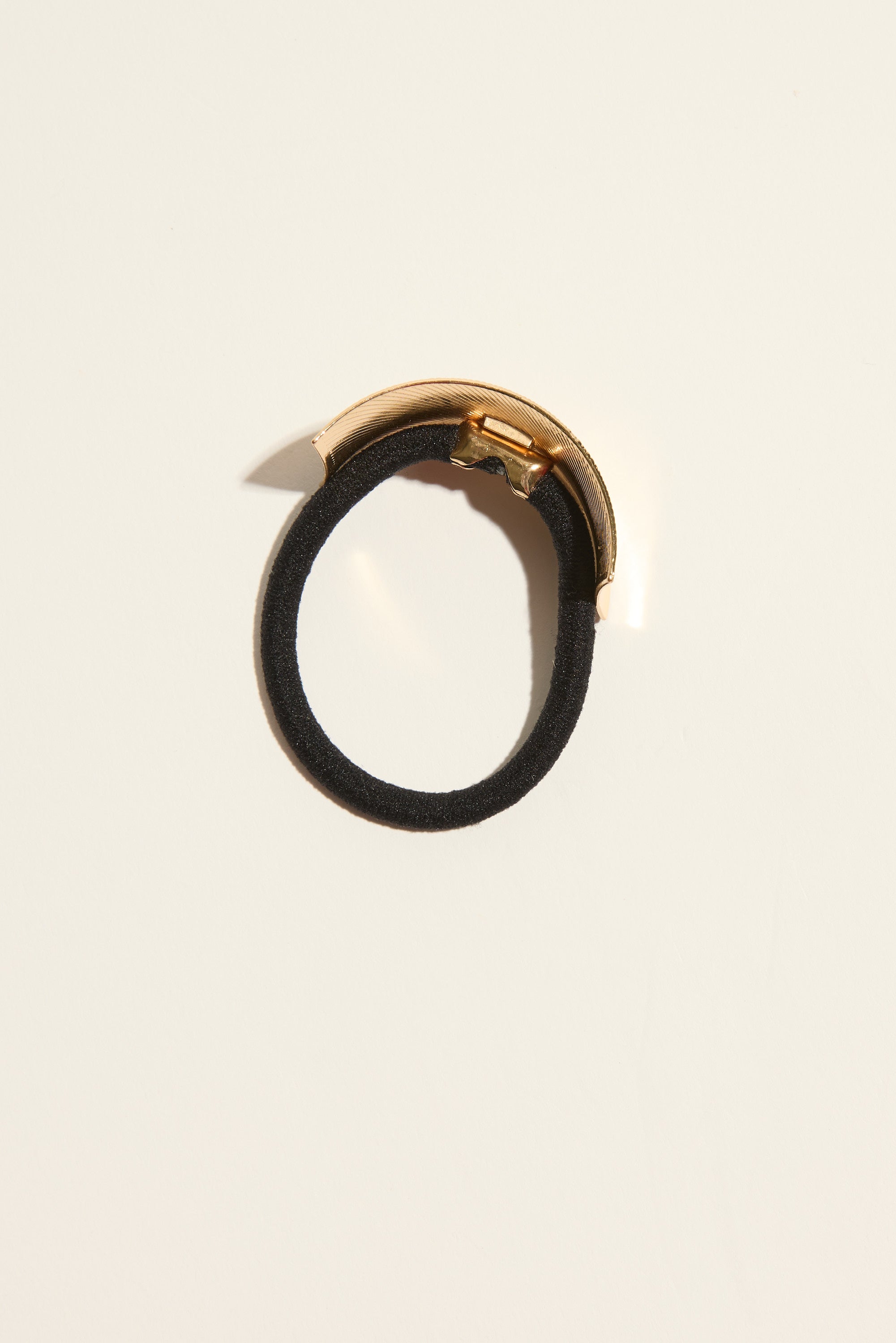 Maeve Textured Metal Hair Tie by Max, black with a gold cuff, on a light beige background.