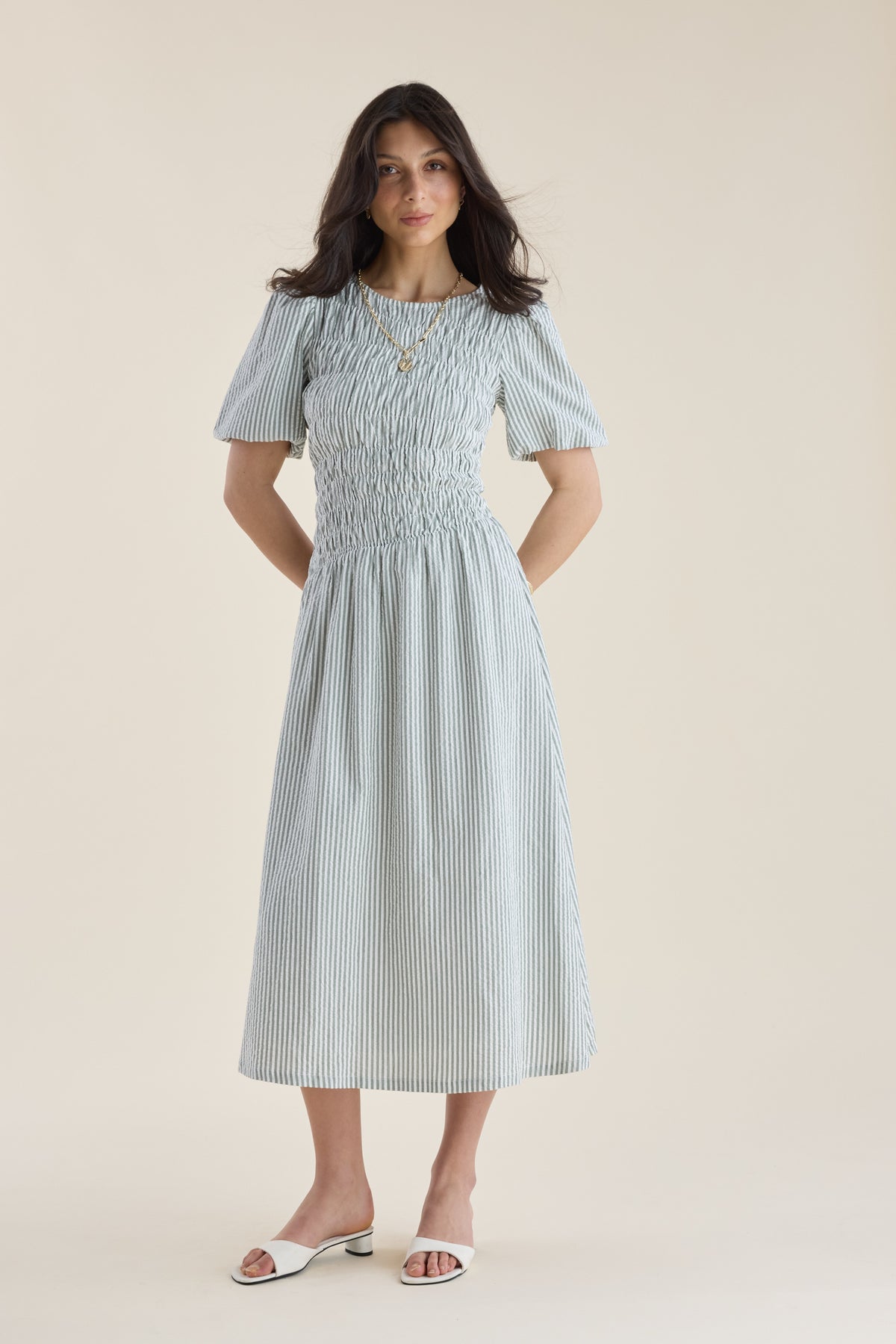 Woman in a Max Talia Shirred Detail Midi Dress with puff sleeves and white sandals.