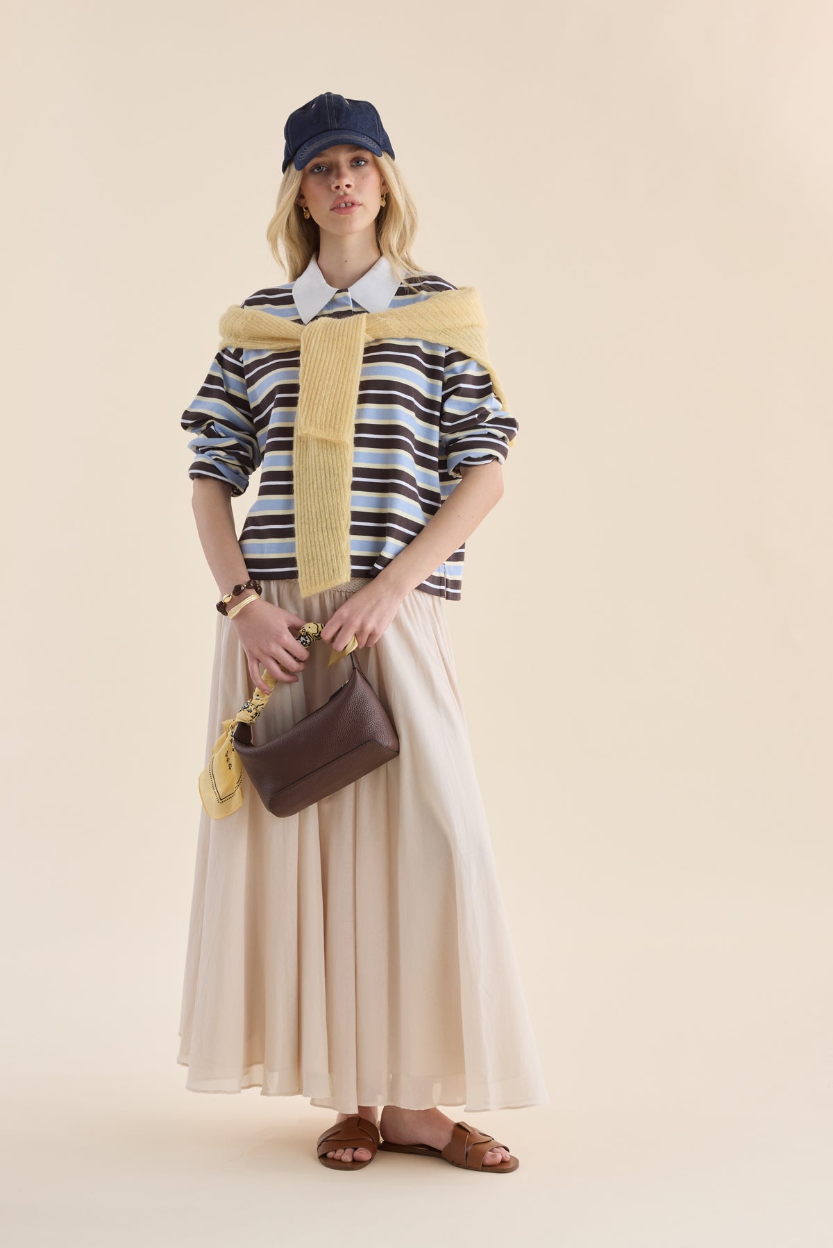 Woman in Elementary Polo Top, cream skirt, relaxed fit, blue cap, carrying brown bag.