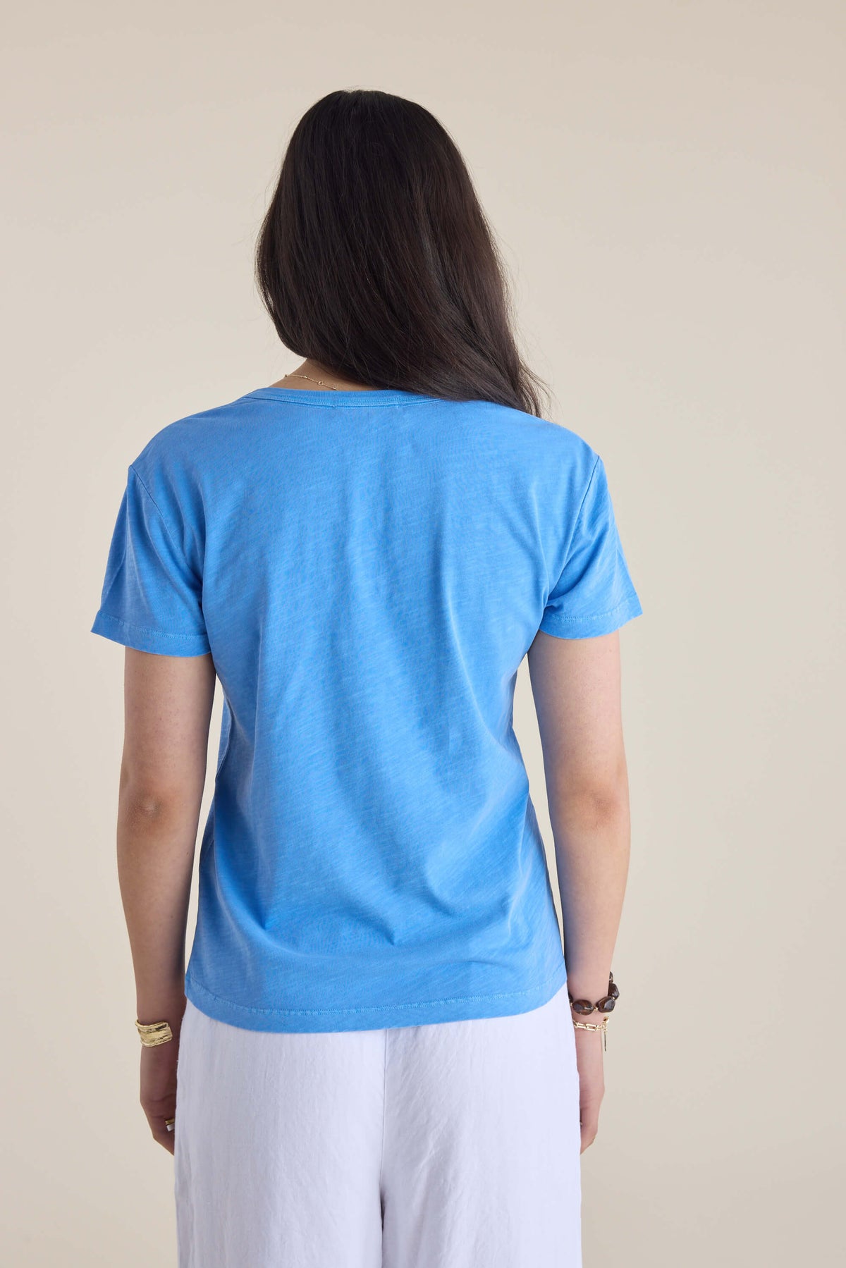 Person with long dark hair in an Elementary Organic Cotton Slub V Neck Tee, back to camera.