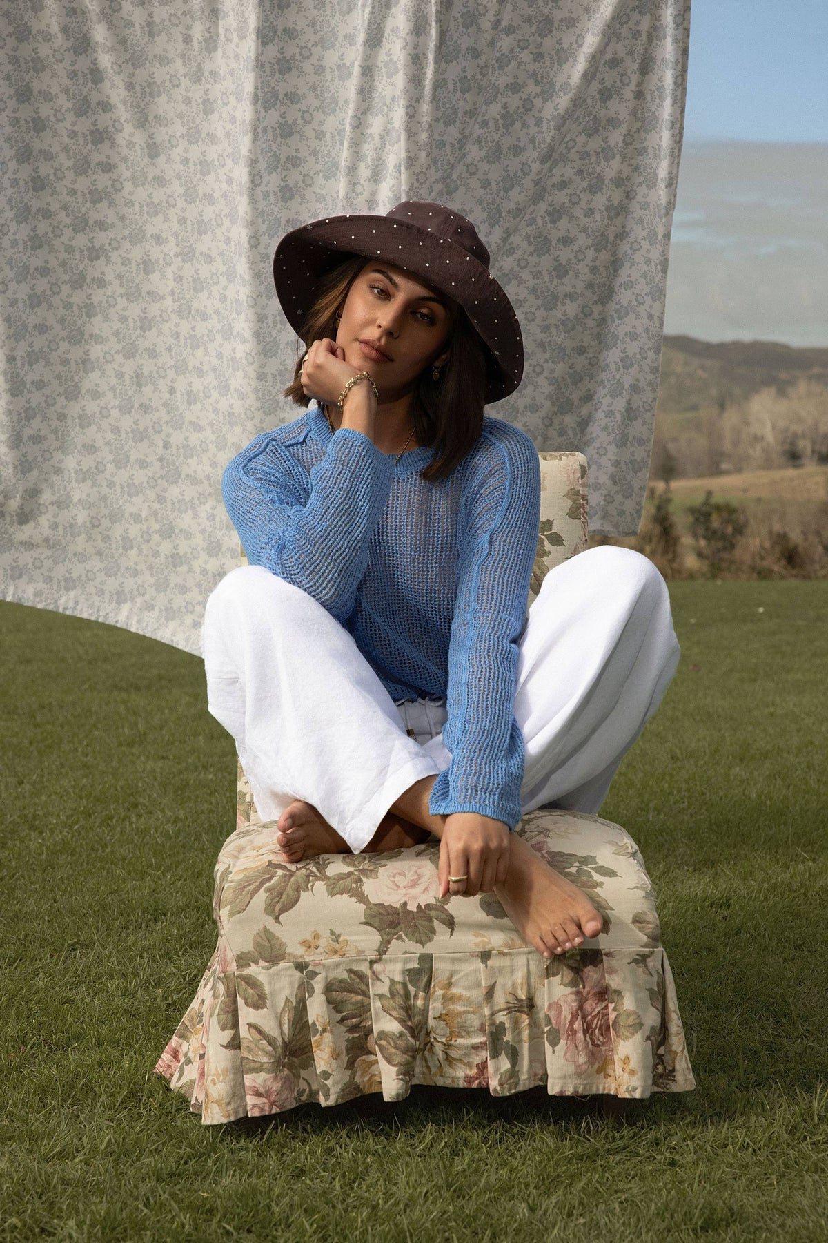 Woman in Elementary Linen Knit Detail Sweater sits barefoot outdoors, curtain behind her.