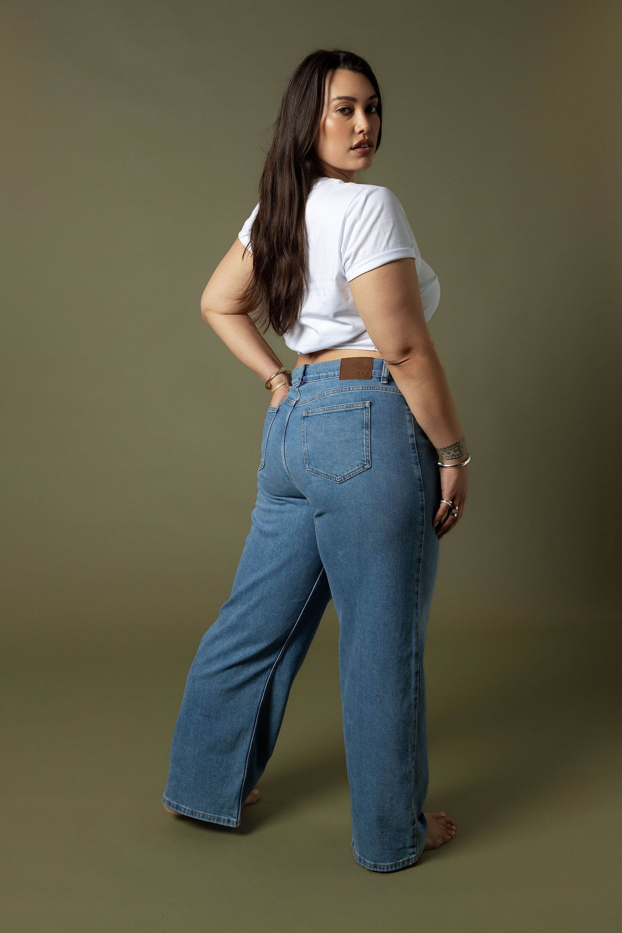 Woman models Max’s Nevada Wide Jeans and a white tee against an olive green background.