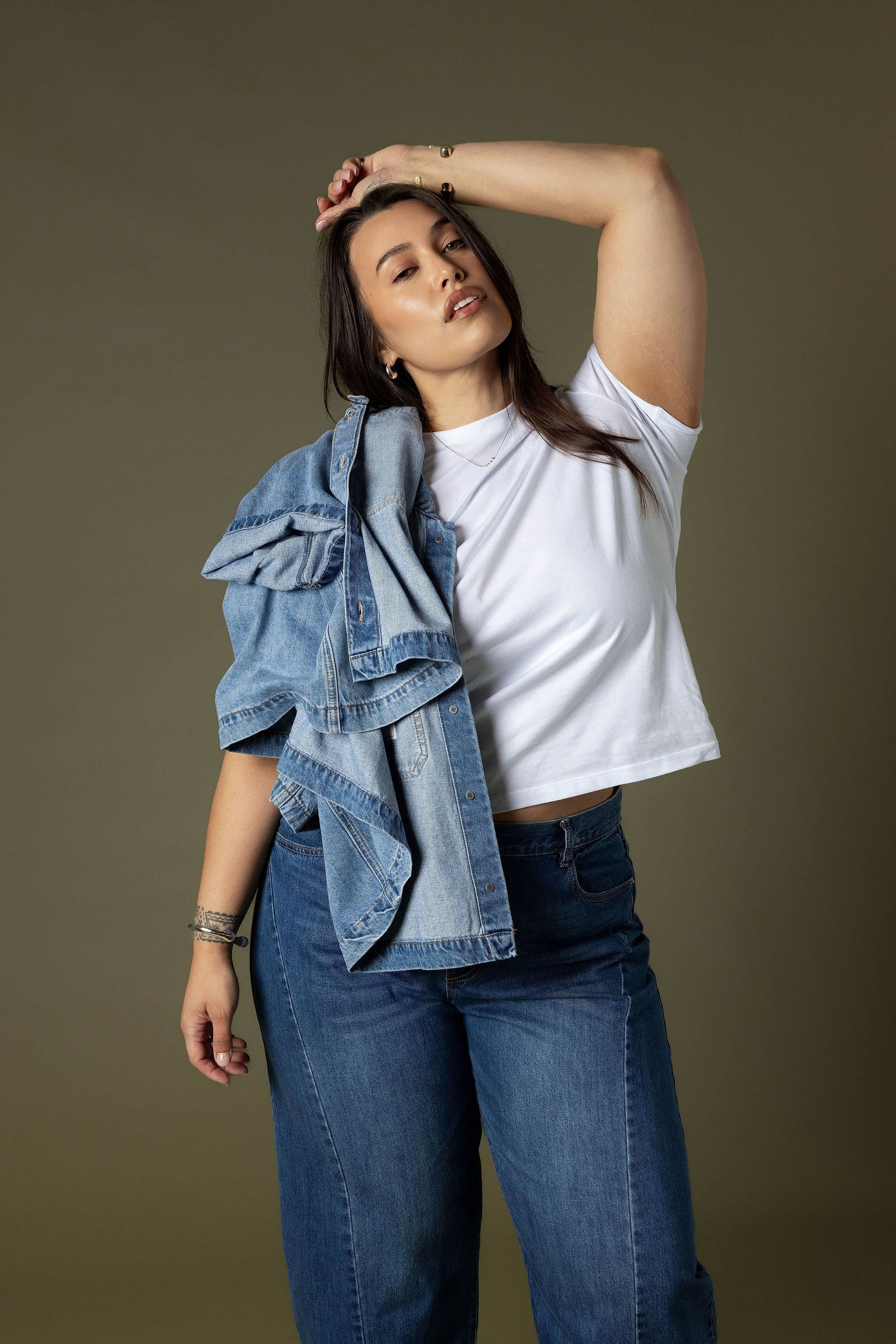 Woman in Max Montreal Barrel Leg Jeans, posing with arm raised and holding a denim jacket.