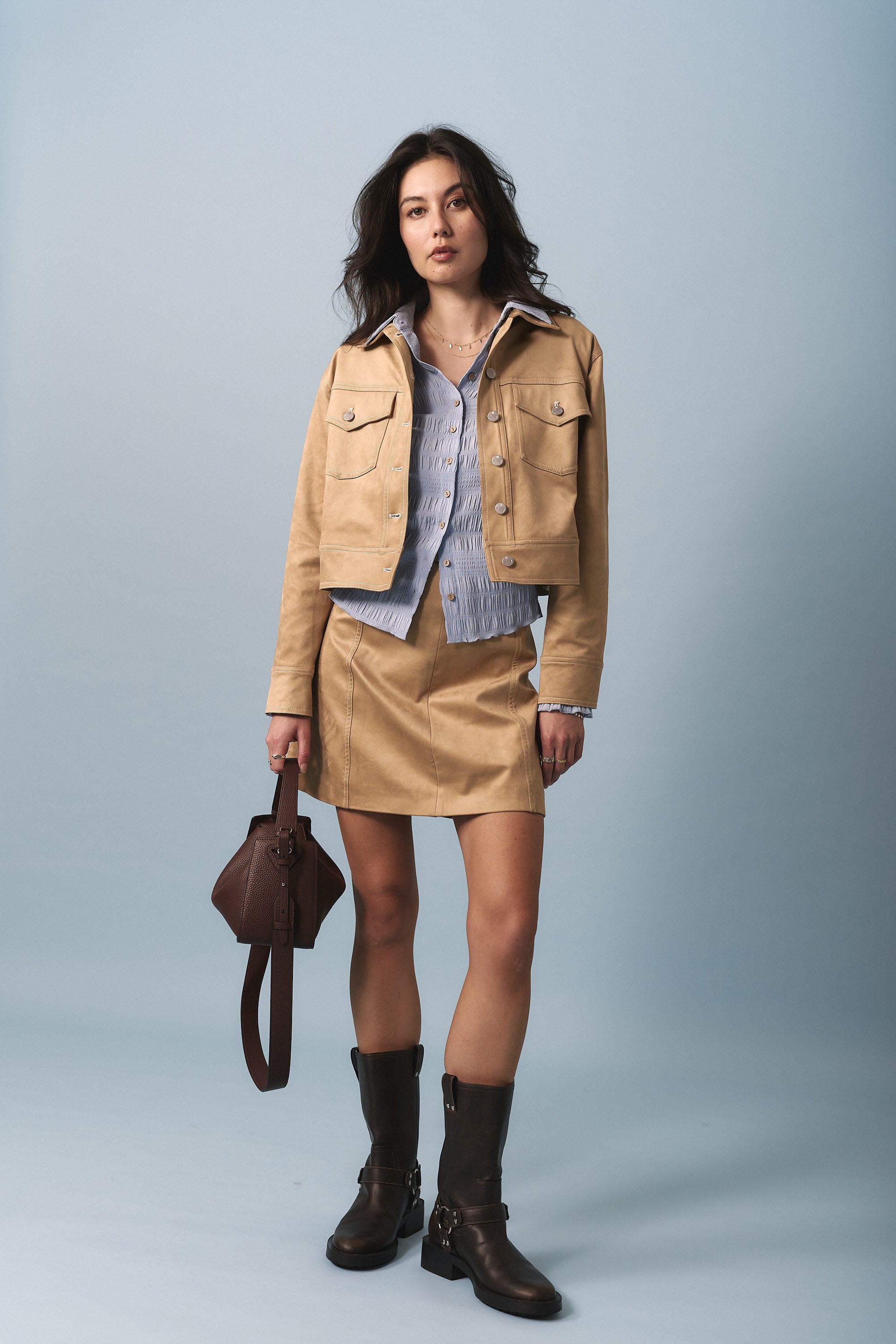 Woman in tan jacket, blue shirt, Portia Suedette Mini Skirt by Max, with brown bag and boots.