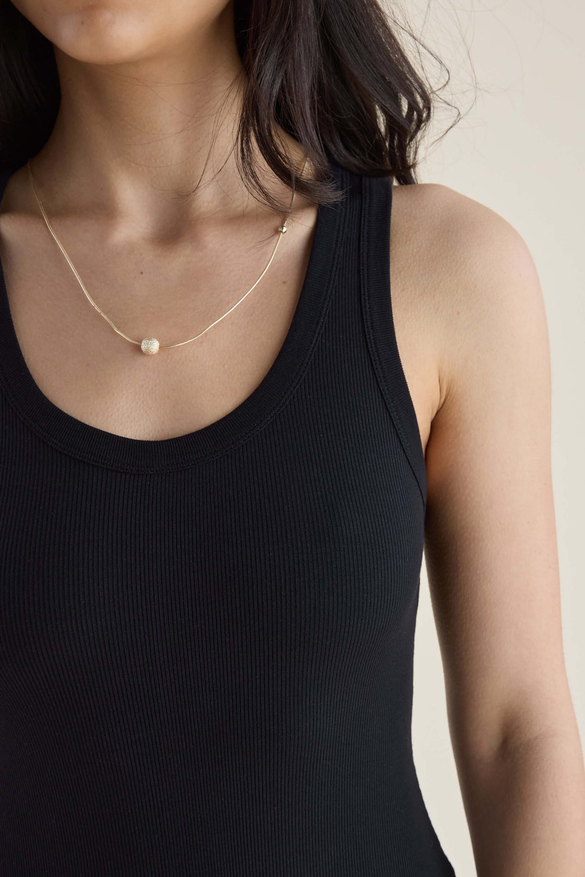 Woman in black Elementary Basics Tank Slip Dress by Elementary, styled with a gold necklace.