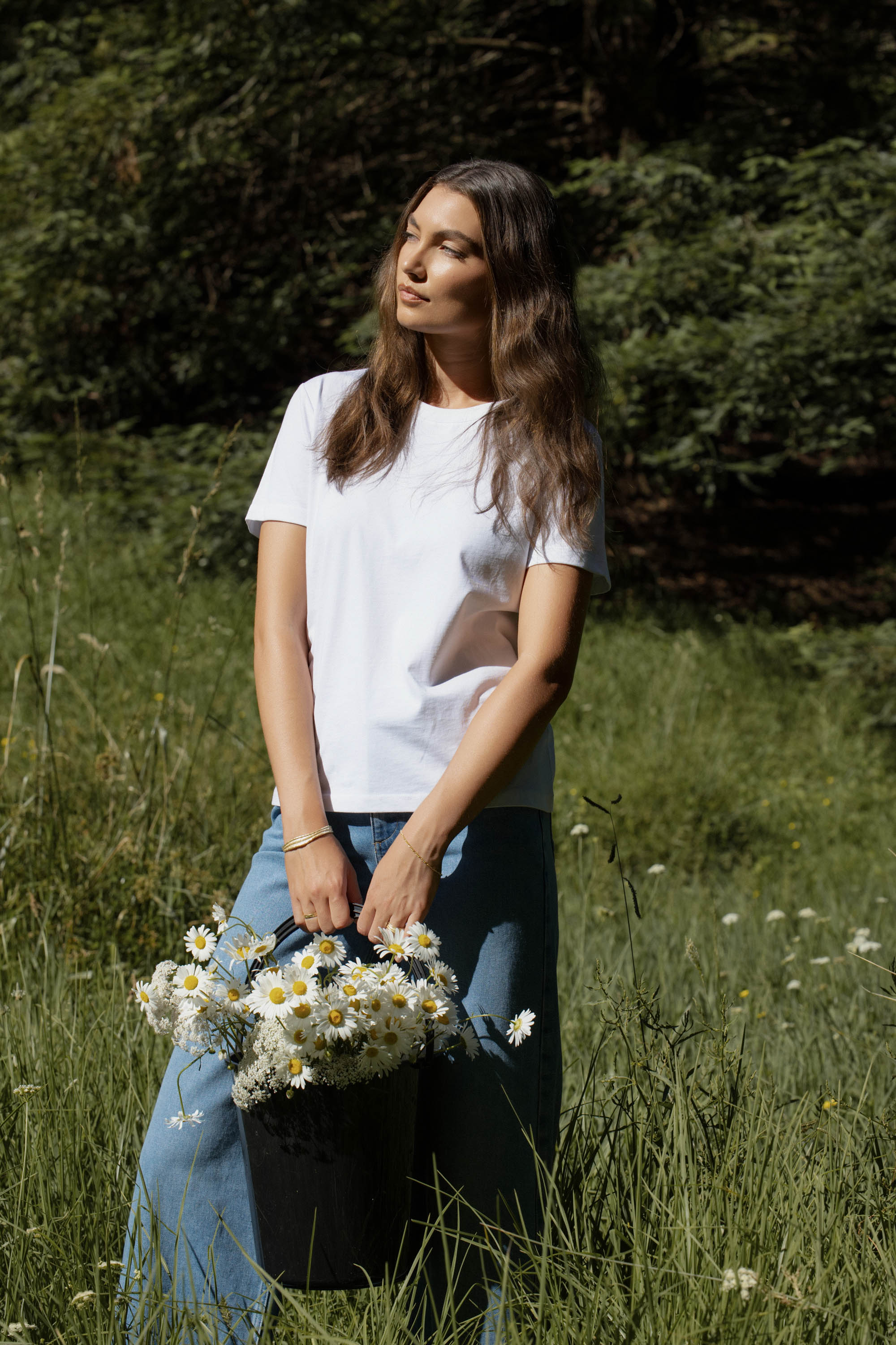 Woman in The Good Earth Cotton Crew Tee by Max, holding daisies in a grassy field.