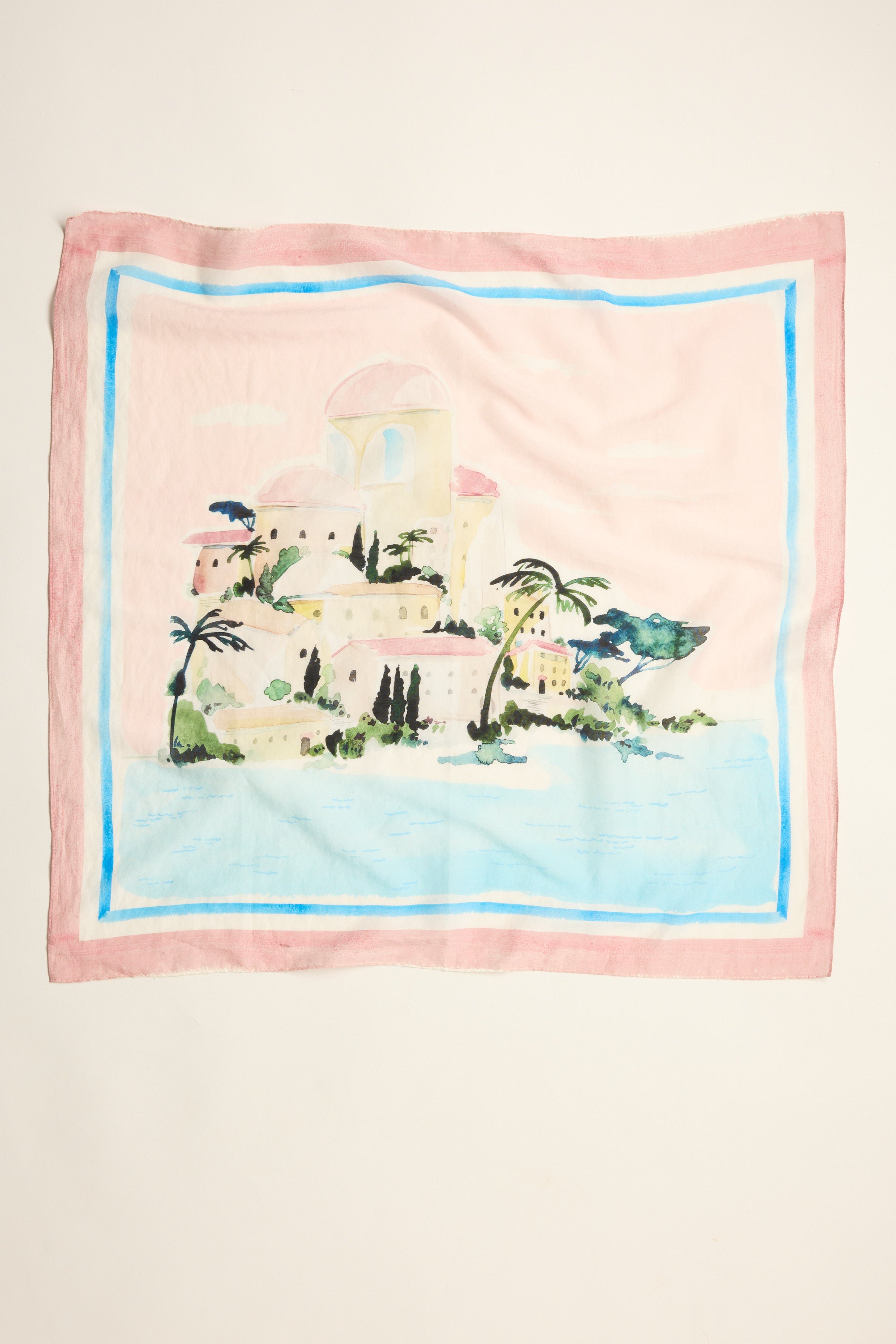 The Portia Silk Blend Square Scarf by Max showcases a hand-painted seaside village with pastel buildings, palm trees, and water on a light background, finished with blue and pink borders—a luxurious accessory.
