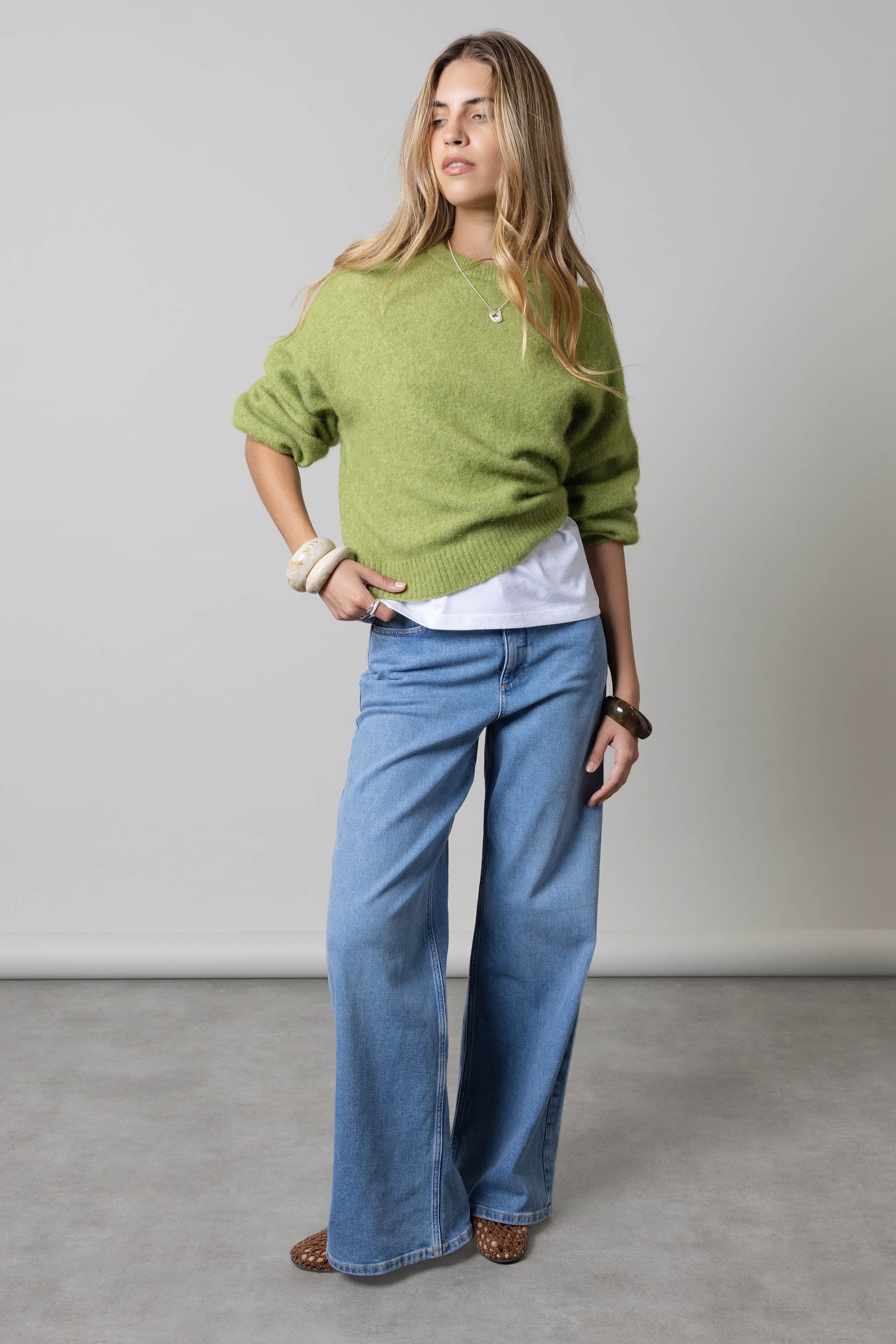 Woman in green sweater and Max Nevada Wide Jeans against a plain grey background.