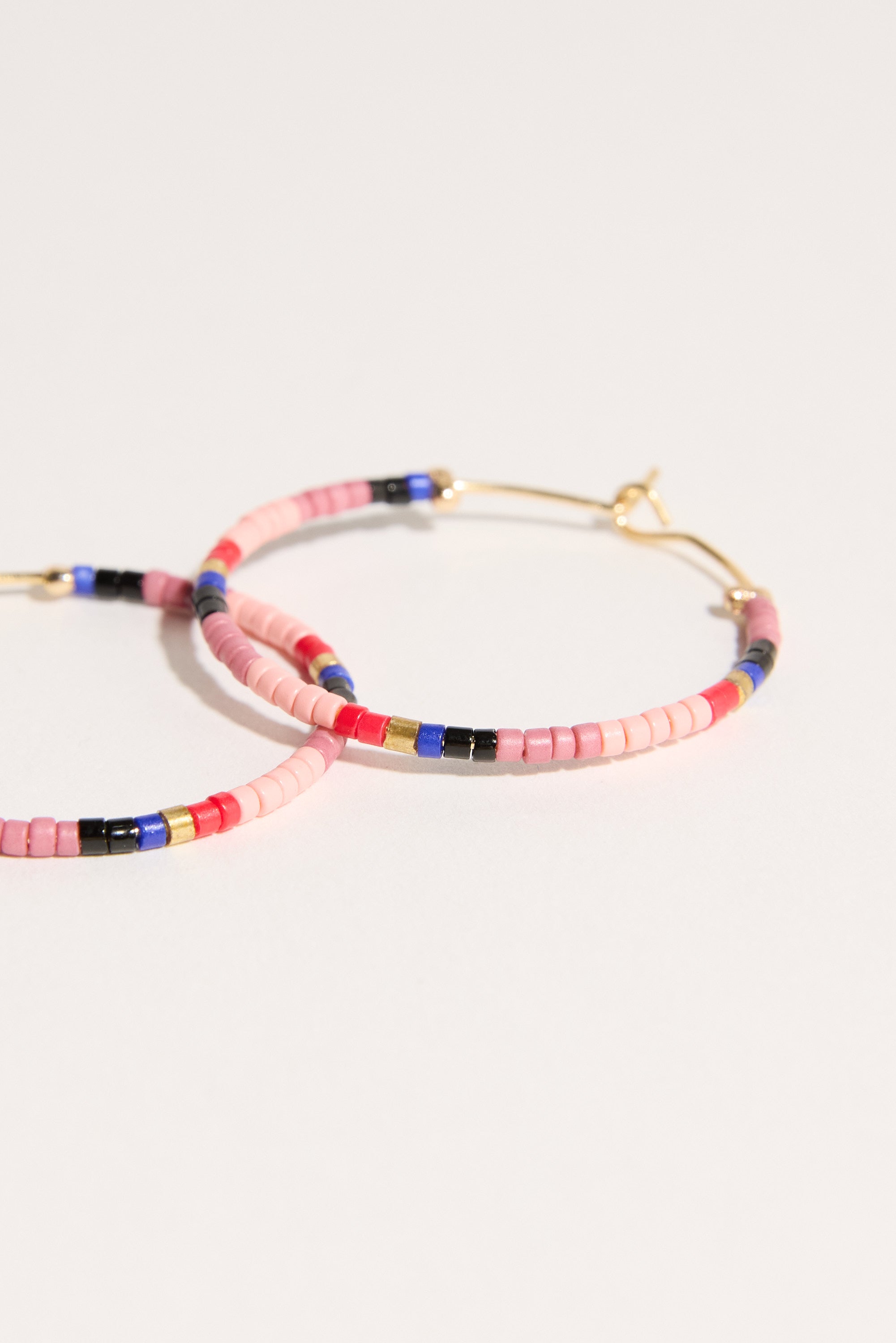 The Bela Sonder Isadora Earrings by Bela Sonder are multi-coloured hoops crafted from recycled brass and adorned with pink, blue, black, and gold glass beads, shown against a light background.