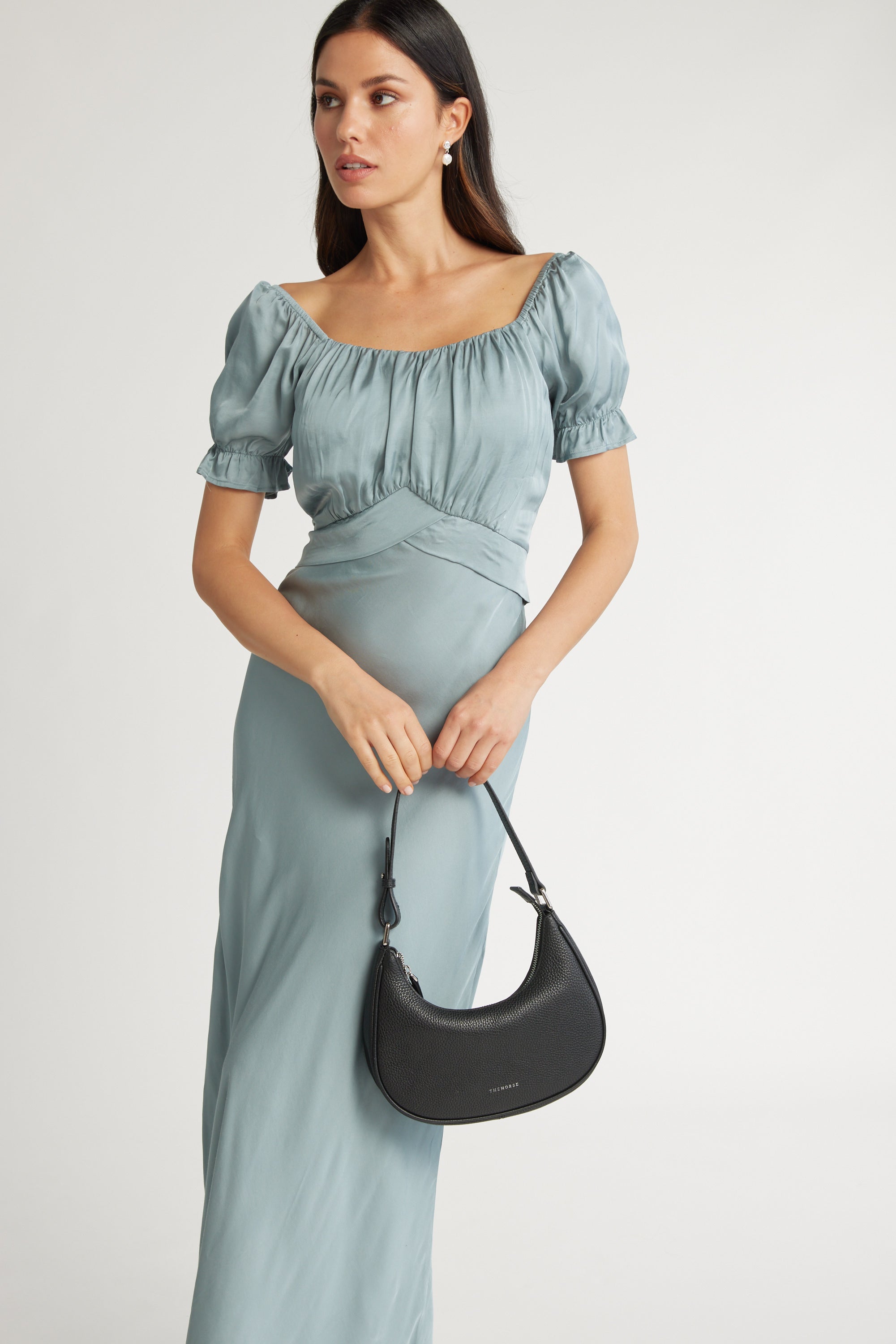 A woman wears the Max Sara Puff Sleeve Dress in light blue, holding a black crescent-shaped handbag with both hands against a plain light background.