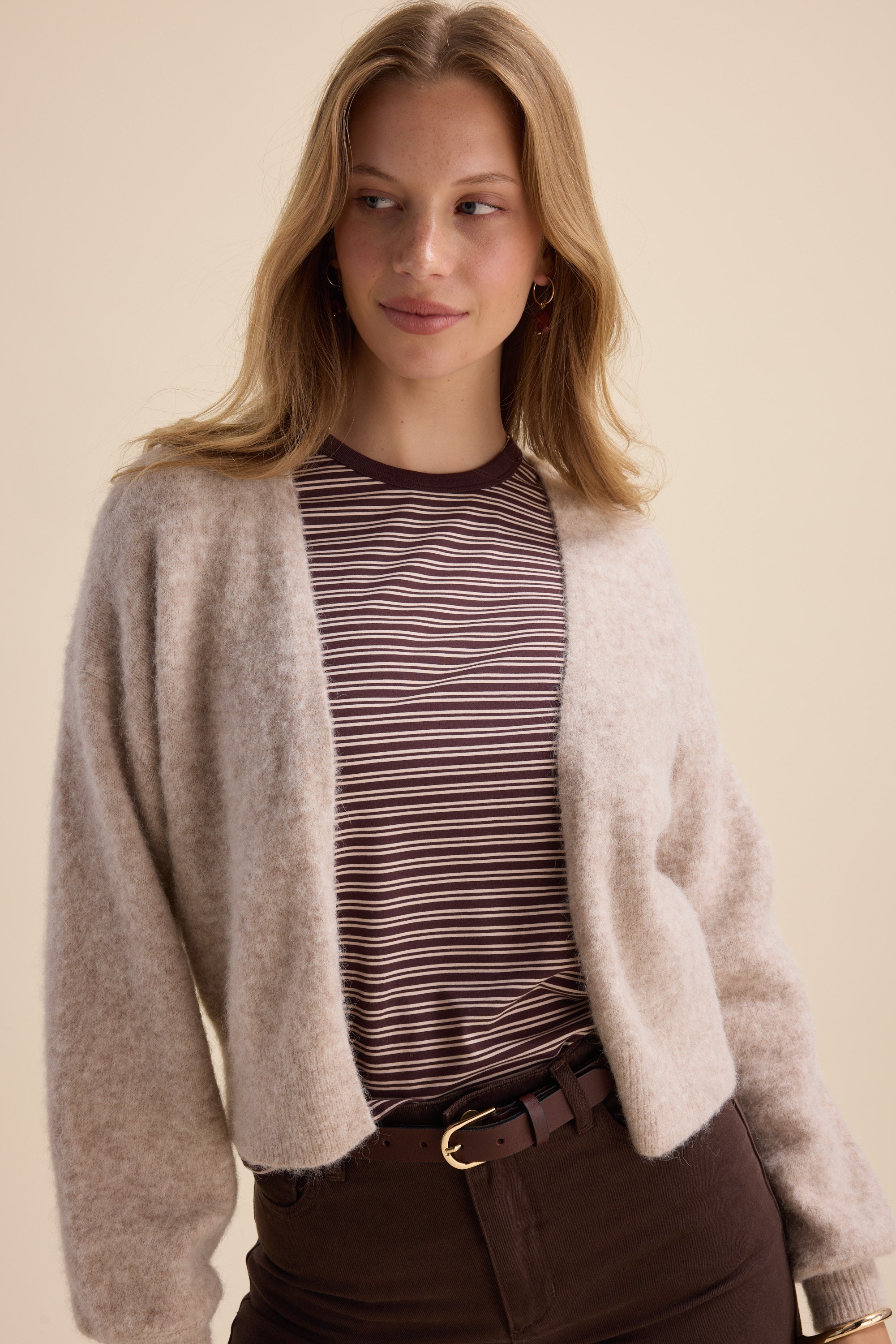 Woman in striped shirt, Max Ultimate Luxe Cardigan, and dark pants smiles looking to the side.
