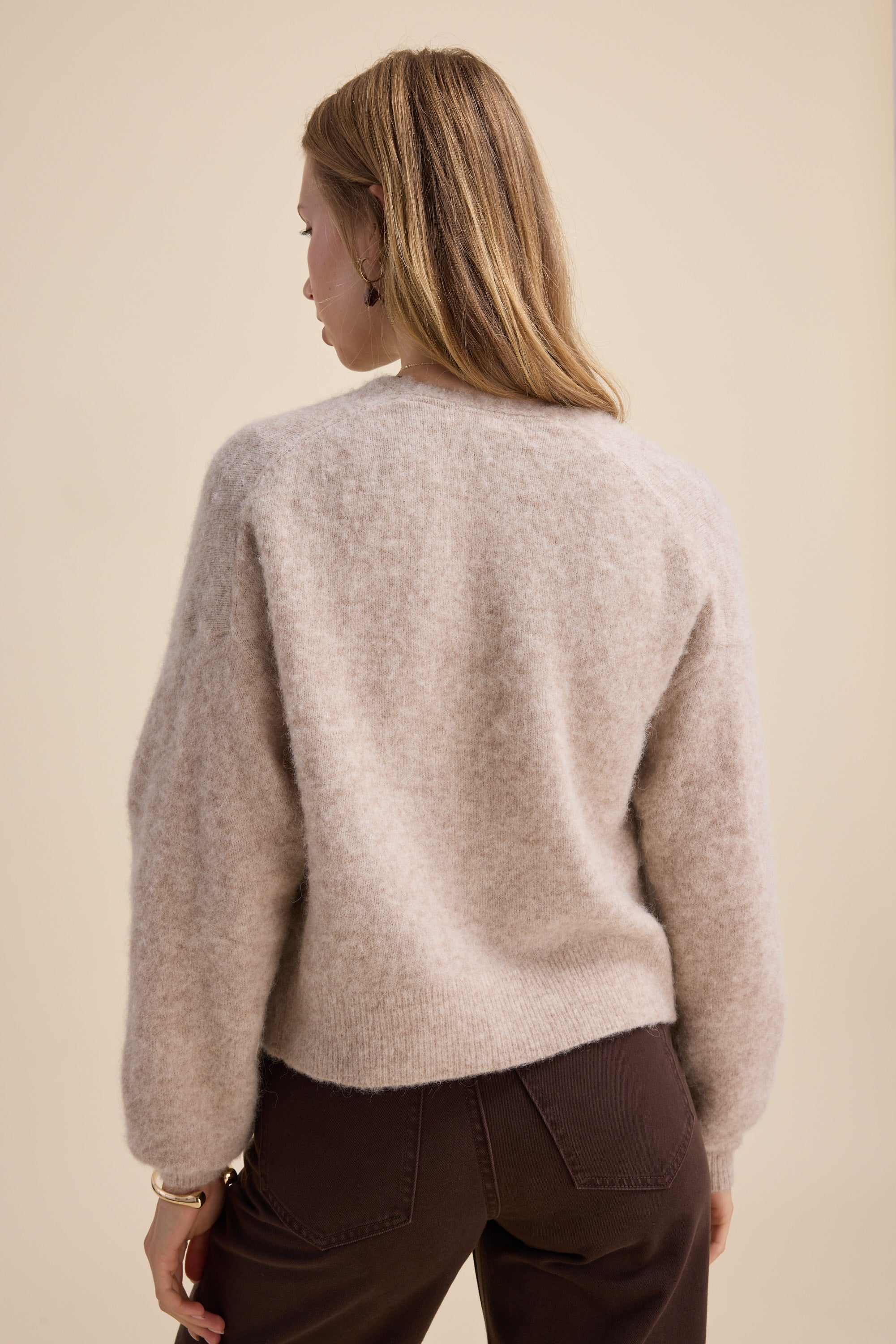 Woman in Max’s The Ultimate Luxe Cardigan, beige, with dark brown pants against a plain background.
