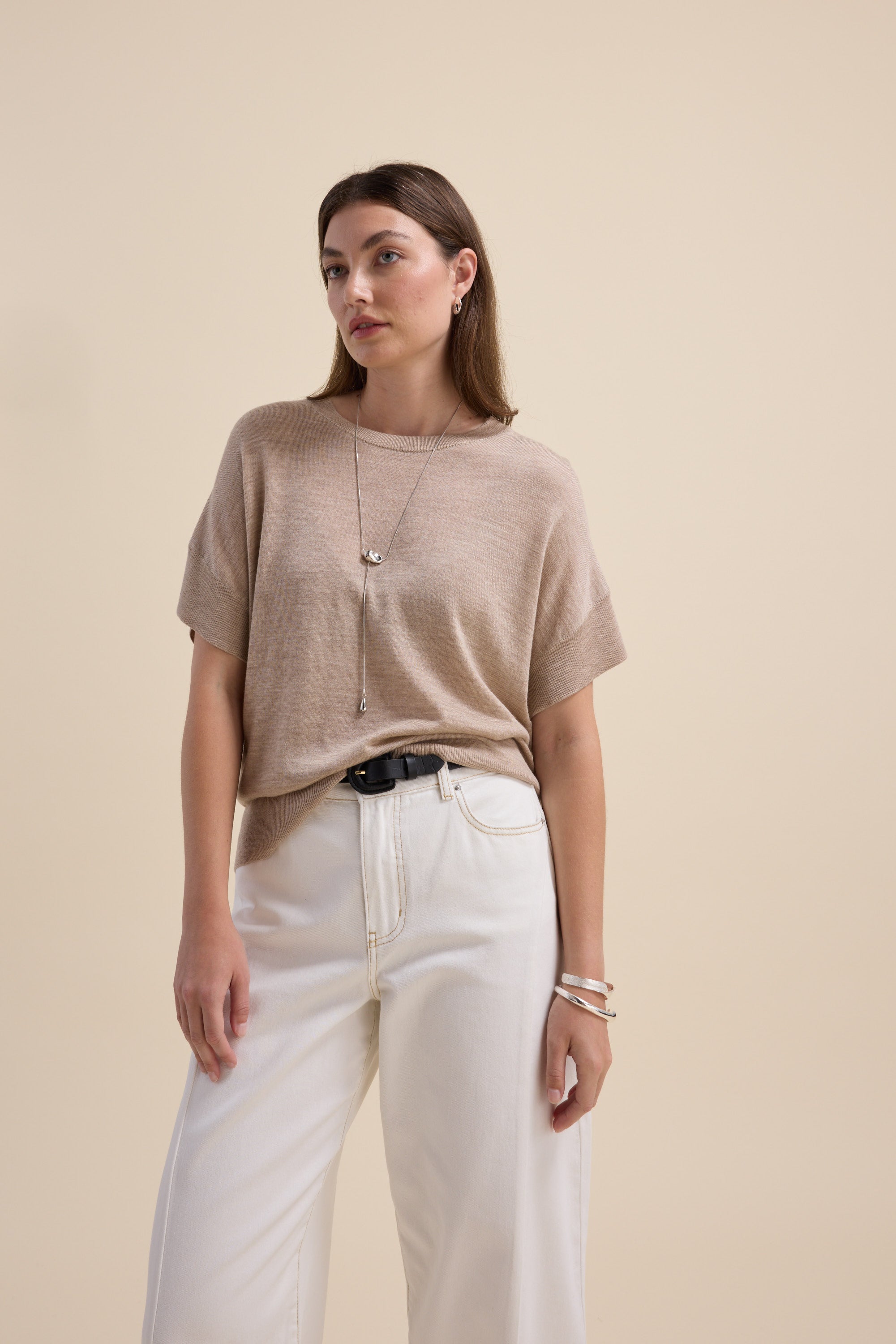 Woman in The Merino Silk Knit Tee by Max and white pants stands against a beige background.