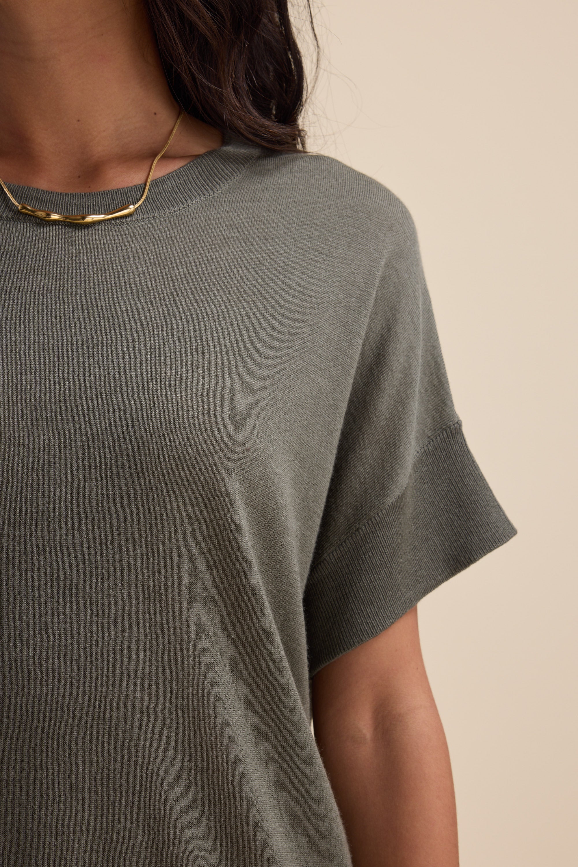 Woman wears Max The Merino Silk Knit Tee in gray, paired with a gold necklace, shoulders up.