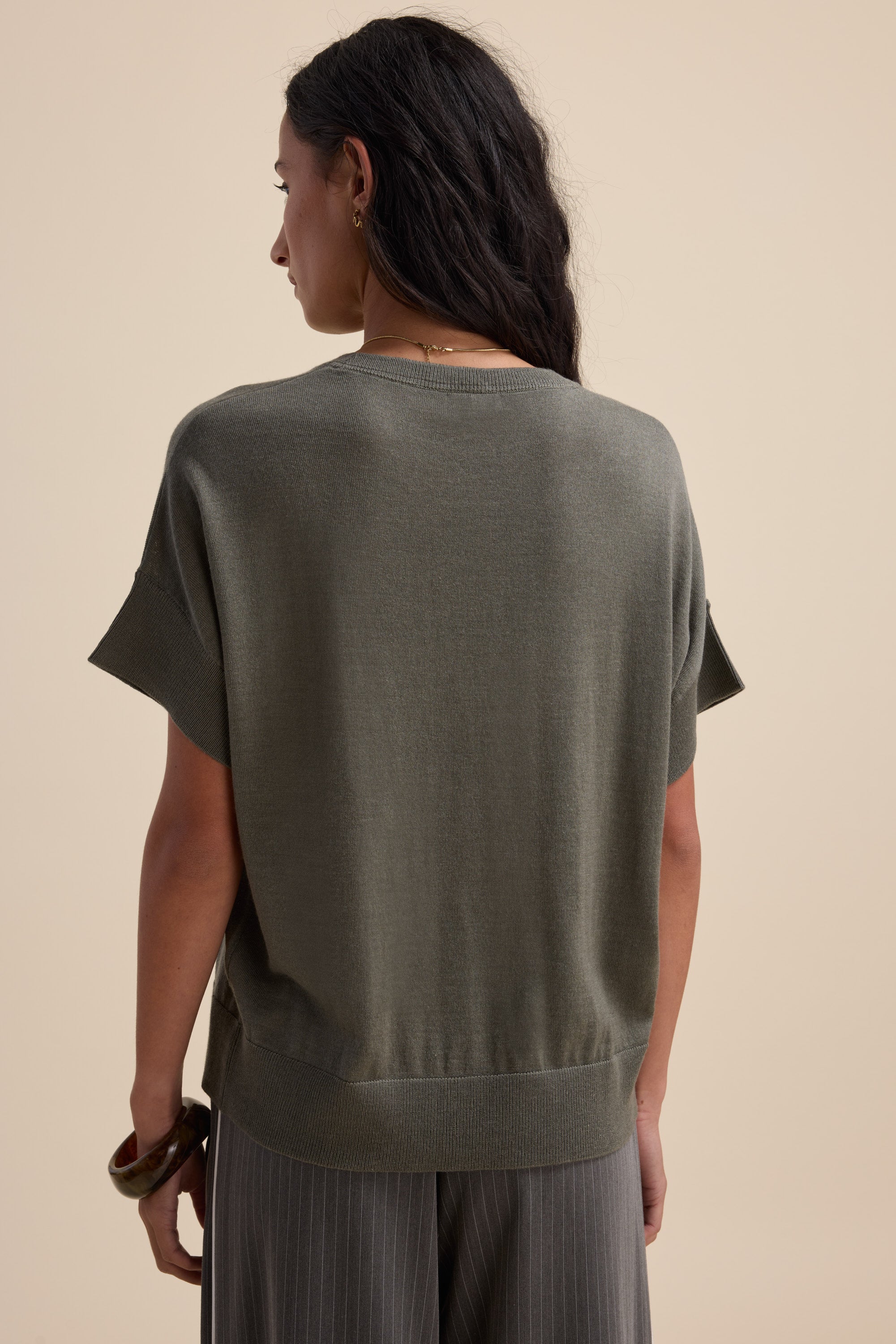 Model in Max's The Merino Silk Knit Tee (olive), back view, on beige background.