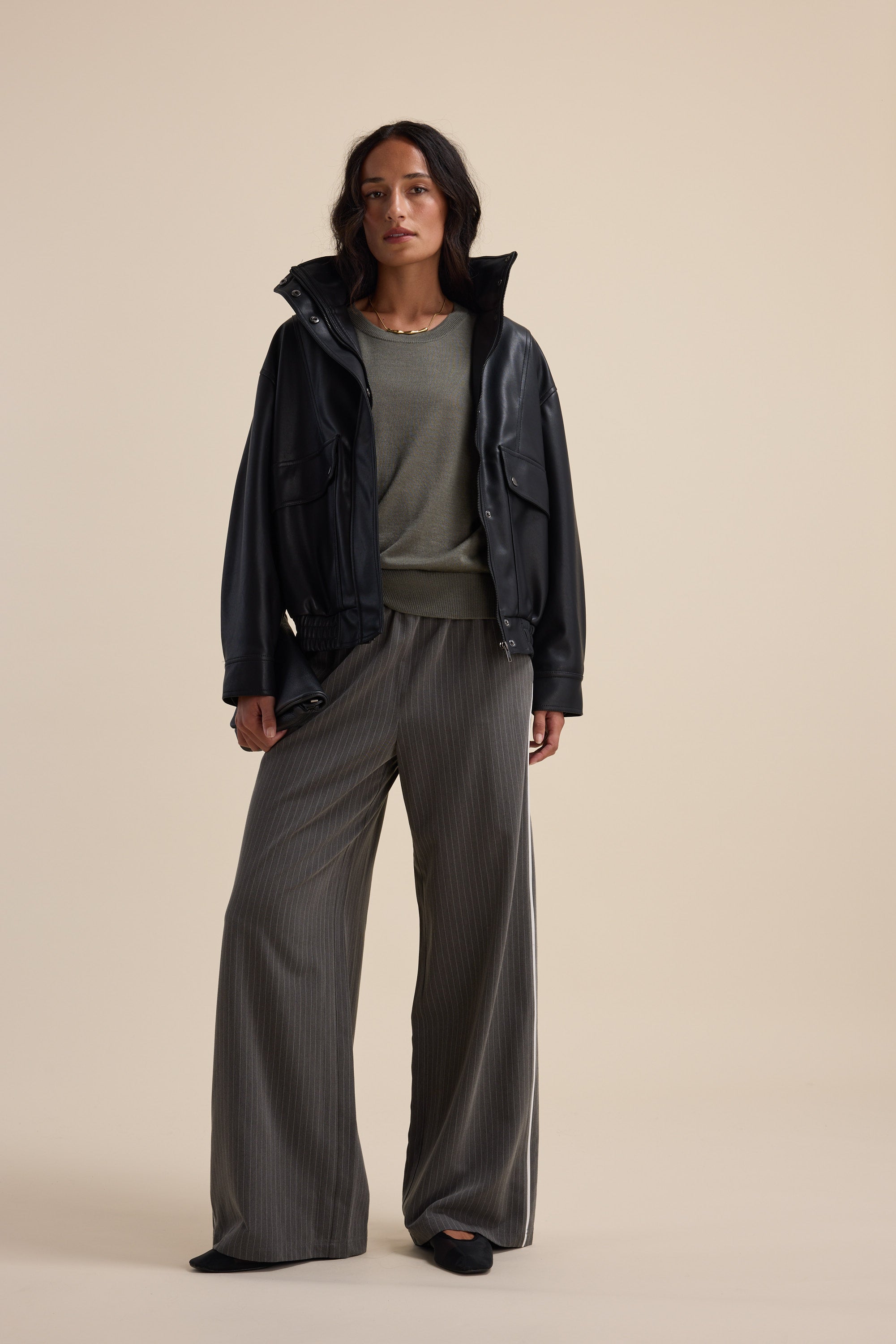 Woman in loose gray pants, black jacket, and Max's Merino Silk Knit Tee against a plain background.