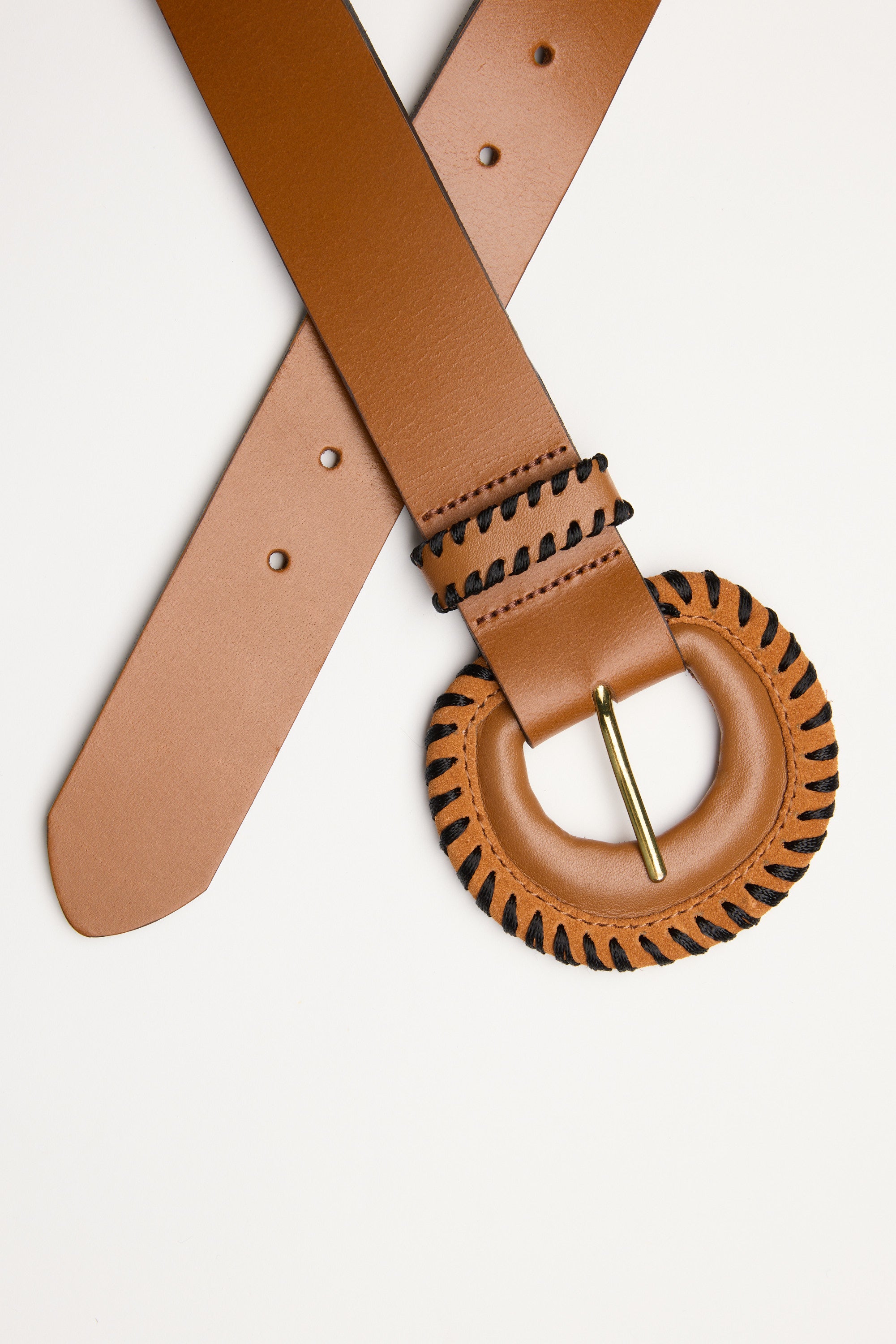 The Contrast Stitch Belt by Max is a tan leather belt made in New Zealand, featuring contrast stitching and a round gold buckle wrapped in black thread, displayed diagonally on a white background with the buckle in focus.