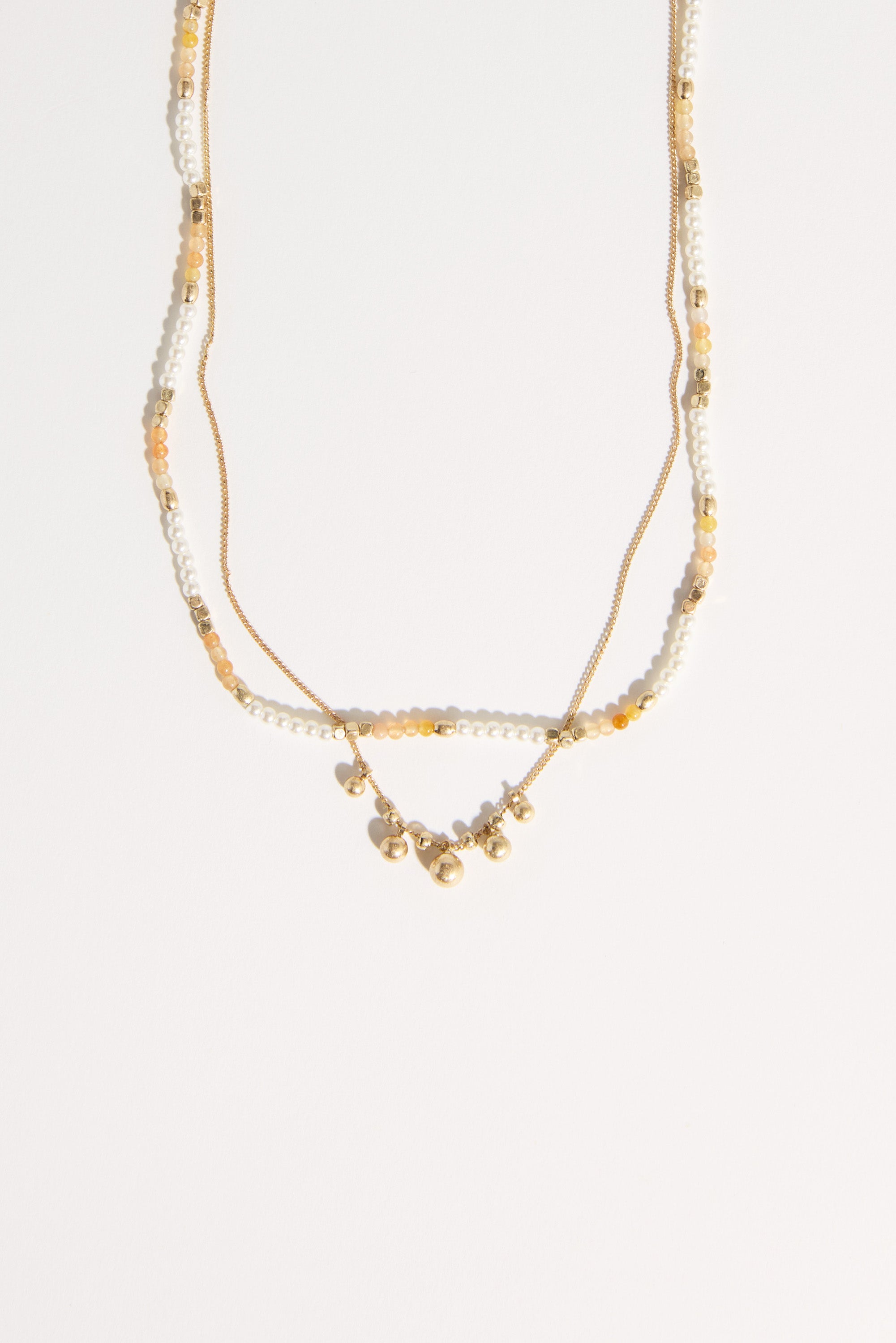 The Bela Sonder Kaia Necklace by Bela Sonder features small gold beads, white pearls, and yellow-orange beads on thin gold chains, shown against a plain white background.
